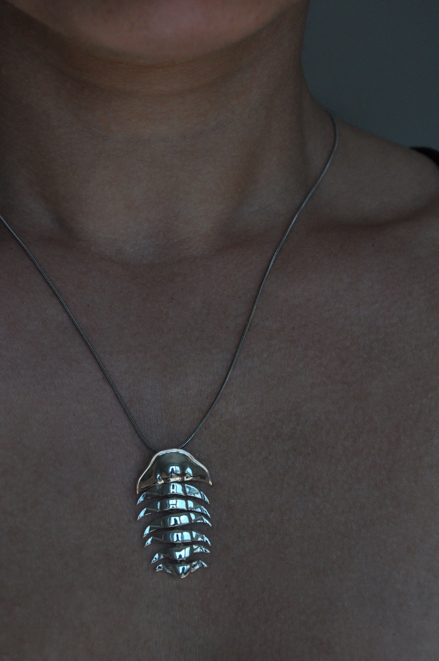 Sterling silver articulated trilobite pendant worn by a model. The pendant rests elegantly against the chest, its segmented design catching light with subtle movement. The polished silver finish contrasts beautifully with the model’s skin tone and outfit, highlighting the fossil-inspired craftsmanship in a wearable, modern form.