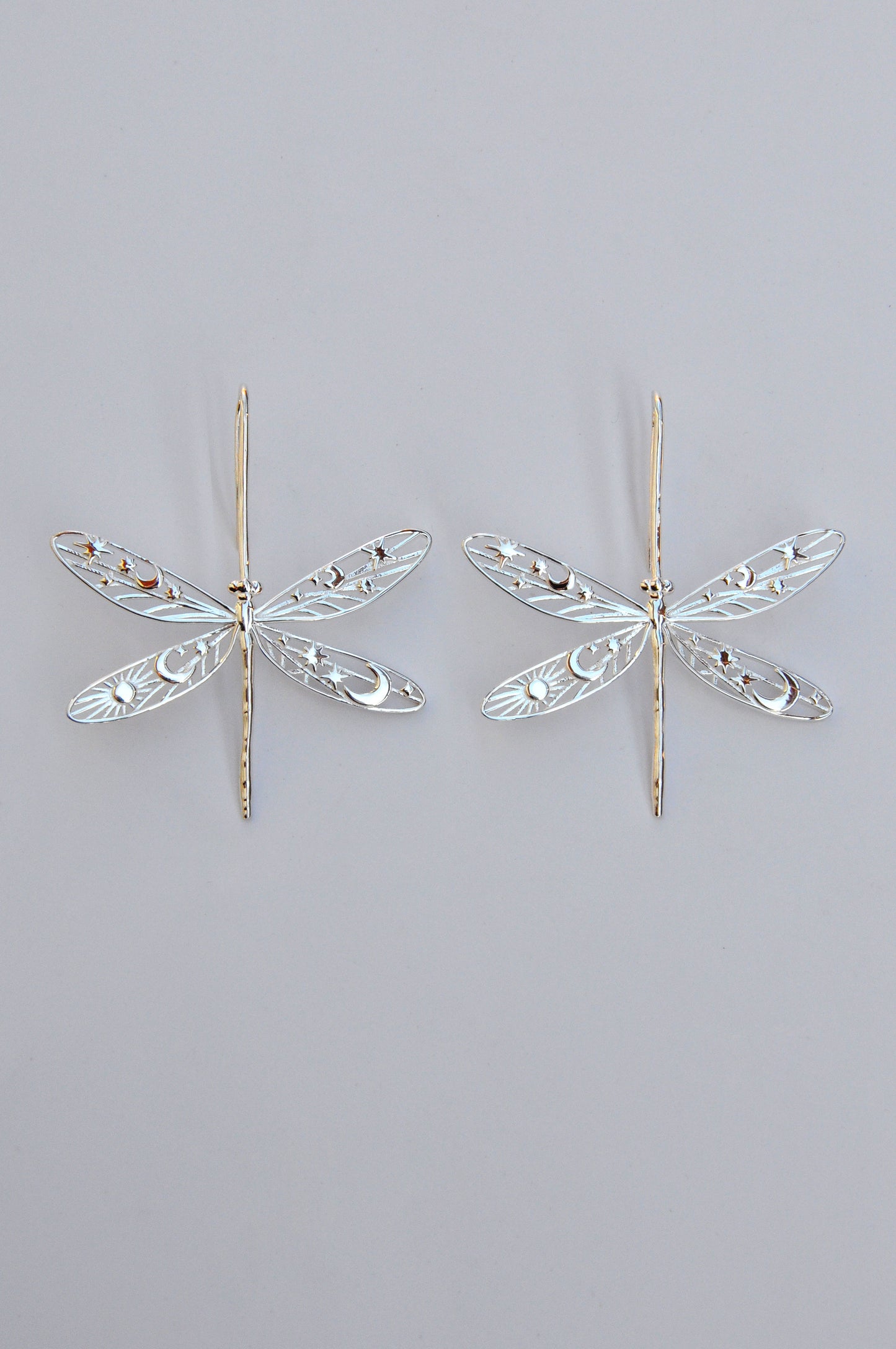 Gold damselfly earrings with intricate celestial cut‑out wings featuring stars, moons, and sun motifs