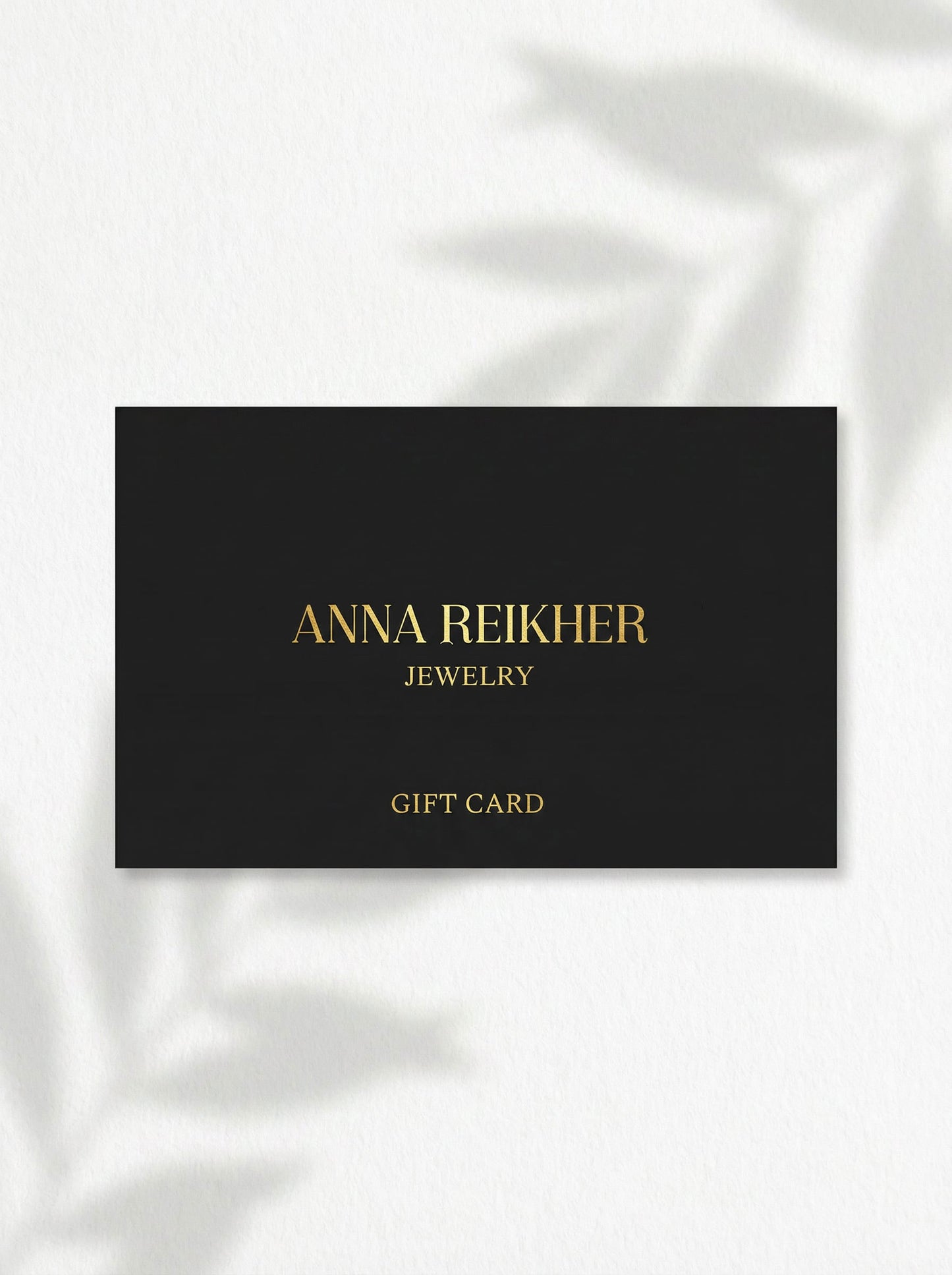 Black and gold Anna Reikher Jewelry gift card photographed on a light surface with soft leaf shadows.