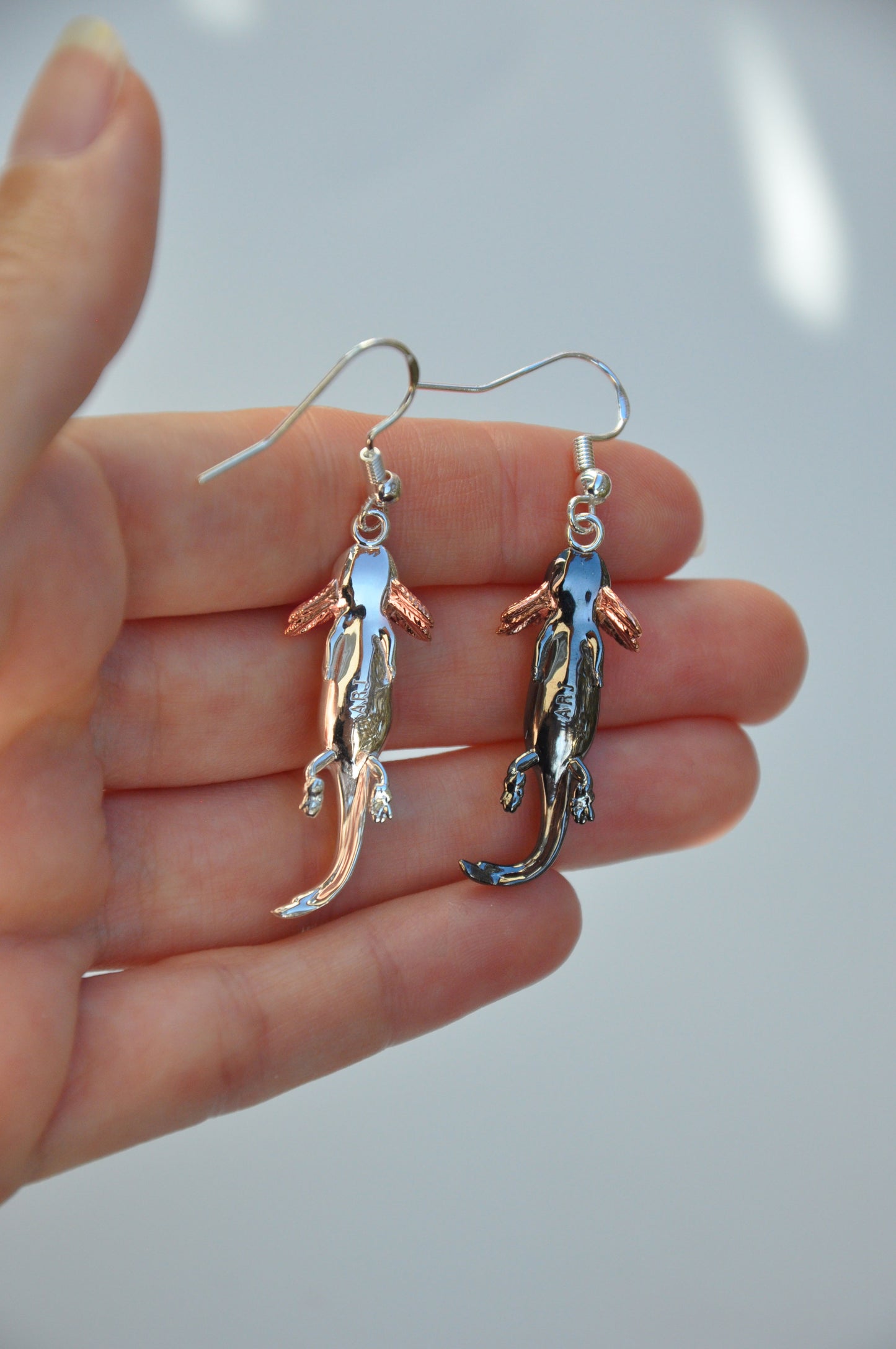 Back side of the Axolotl Drop Earrings held in hand, showing the clean finish and subtle curvature of each piece.