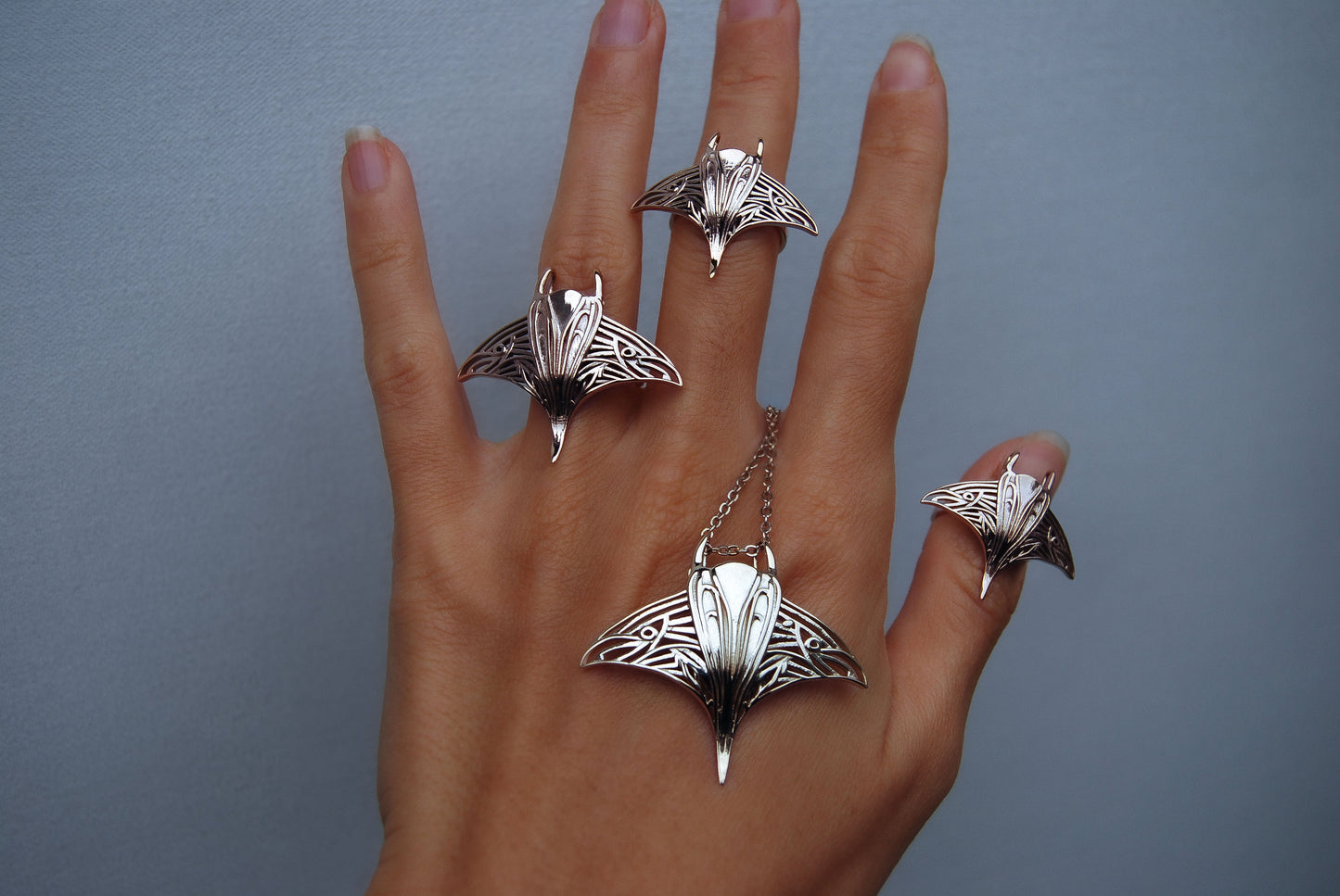 Hand adorned with manta ray pendants and rings in mixed metals, showcasing ocean jewelry collection.