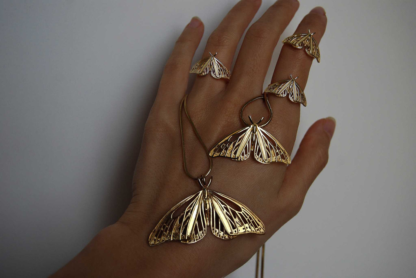 Gold Monarch Butterfly pendants and matching rings displayed on a hand, showing sculptural openwork wings and polished finish.