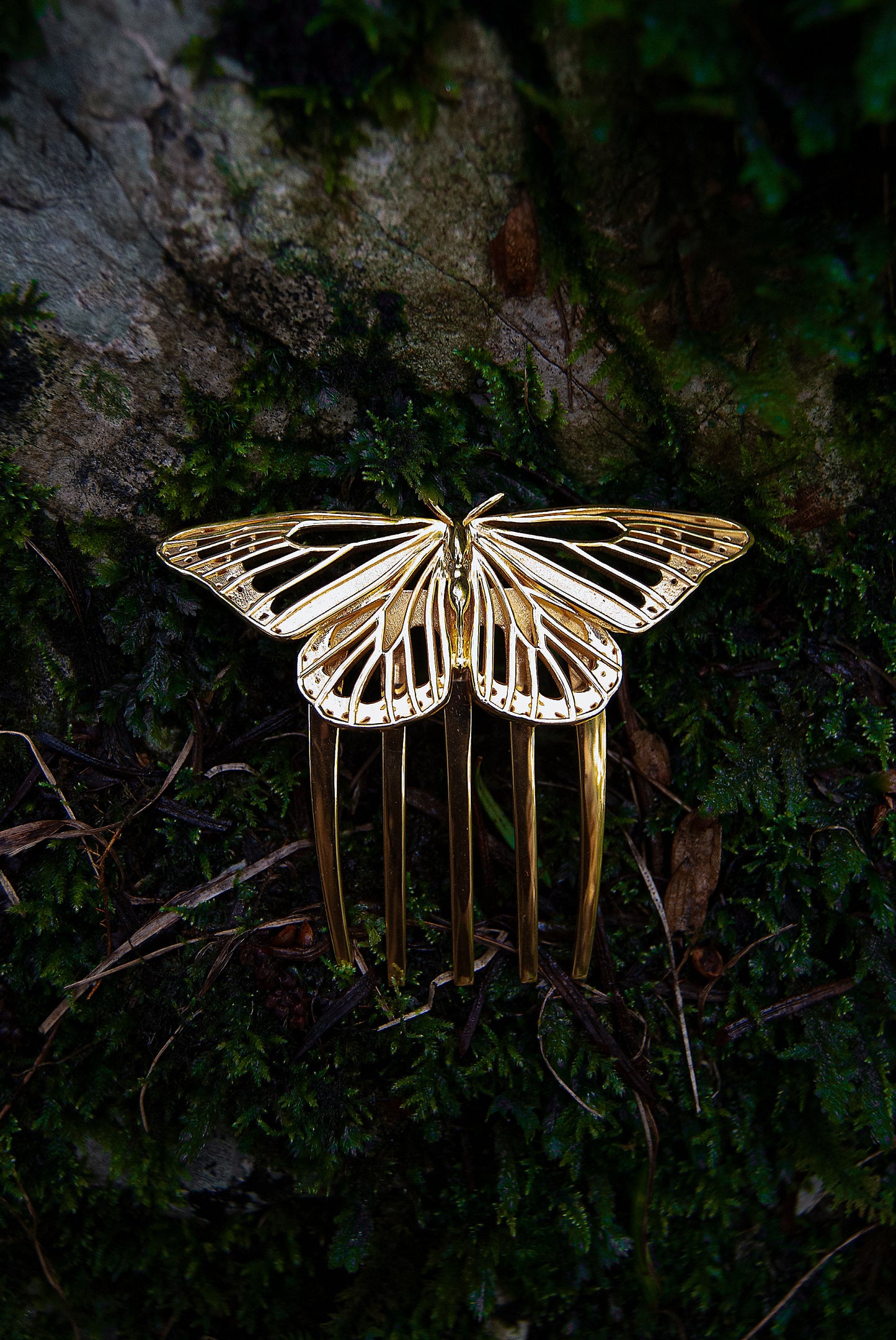 Front view of a 14k gold plated Monarch Butterfly hair comb set against a lush forest backdrop. The comb’s radiant wings gleam in natural light, echoing the elegance of woodland creatures and blending seamlessly with the organic textures of moss, bark, and leaves.