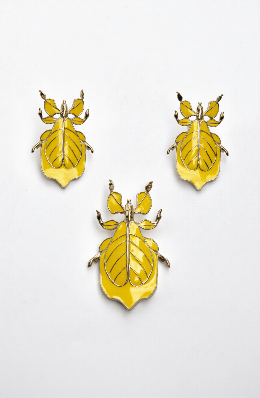 Three Phylliidae leaf‑inspired stud earrings in yellow enamel with gold outlines, arranged on a white background.