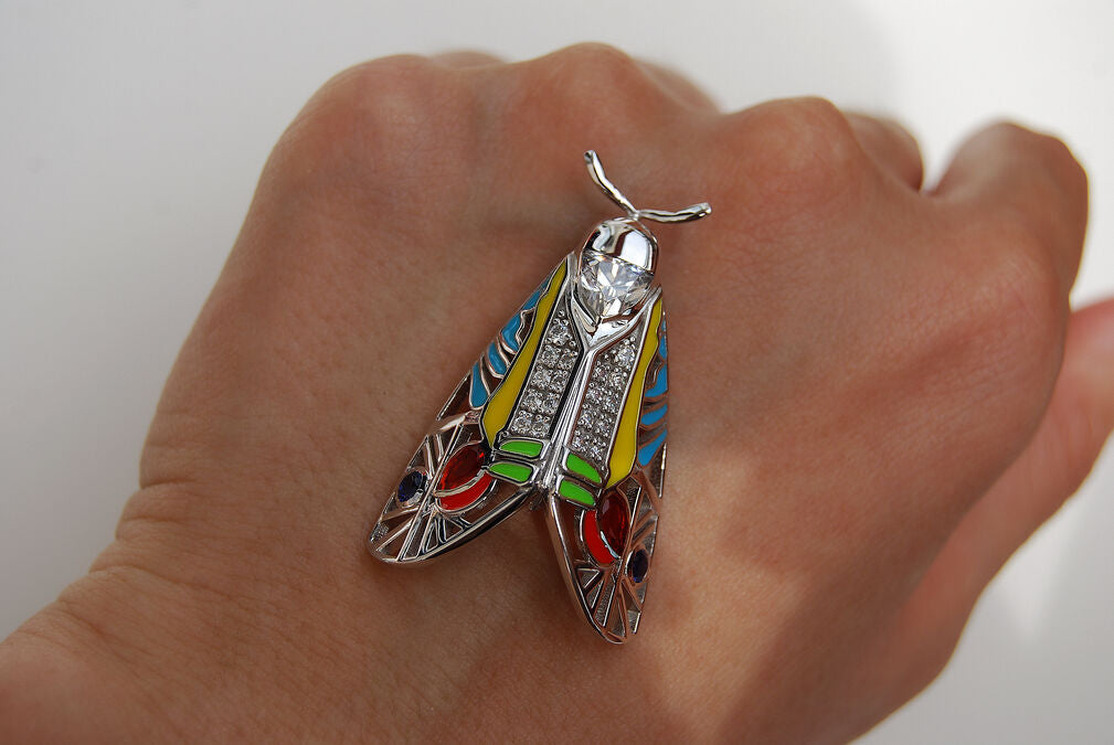 Zoomed-in close-up of Picasso Moth pendant with colorful enamel and zirconia stones resting on hand against white background