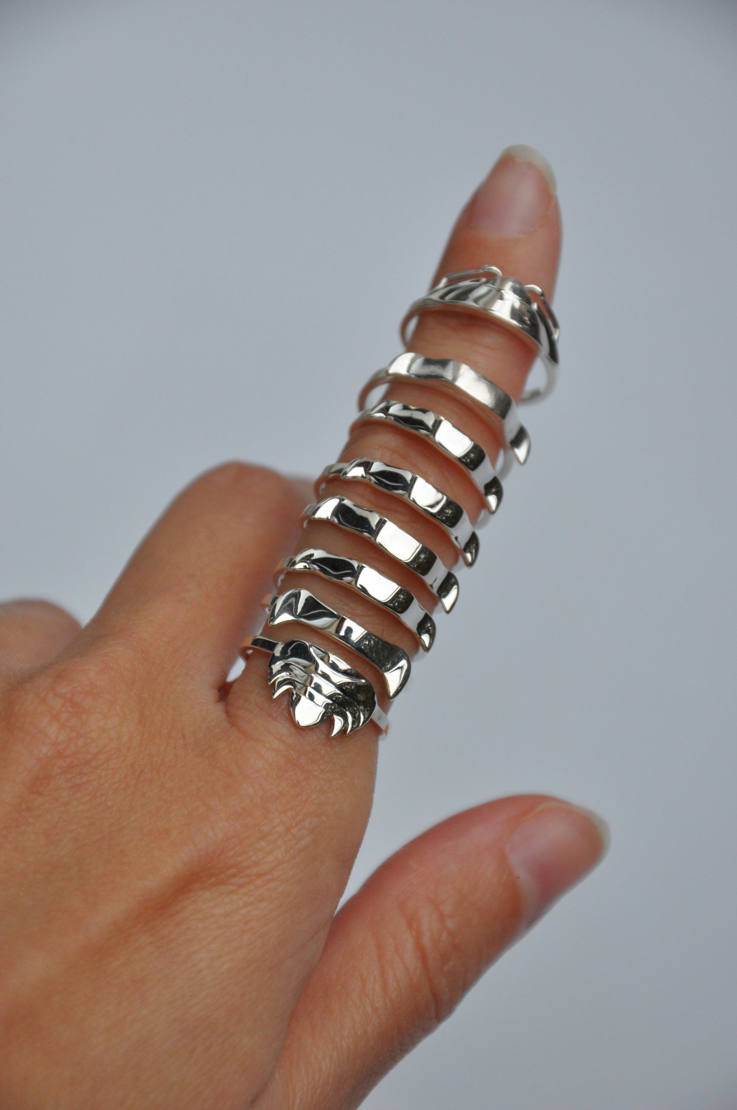 Finger wearing separated silver isopod rings, showcasing modular stacking design and segmented form.