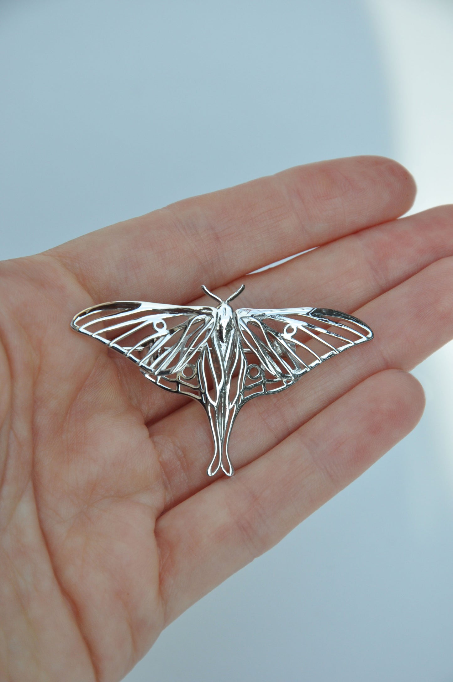 Front view of the silver Luna Moth brooch worn on a hand, displaying its size and intricate design.