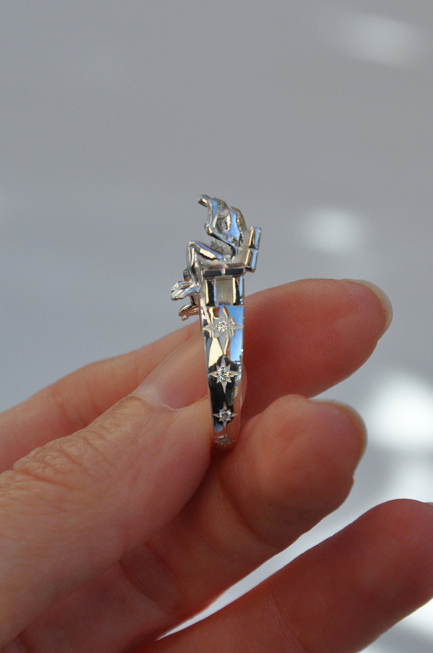 Miniature sculptural ring featuring two tiny frog figures on a platform with dark inlay segments and hand‑set crystal stars.