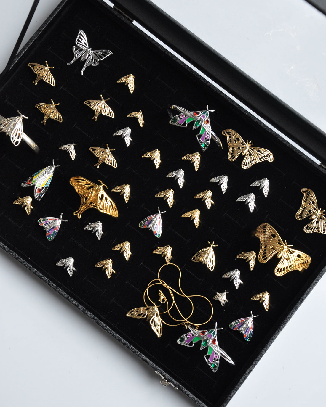 Jewelry box displaying a curated moth-inspired collection featuring sphinx, hawk, tiger, and death's-head motifs. Pieces crafted in gold, silver, and rose gold, with intricate enamel detailing and gemstone accents