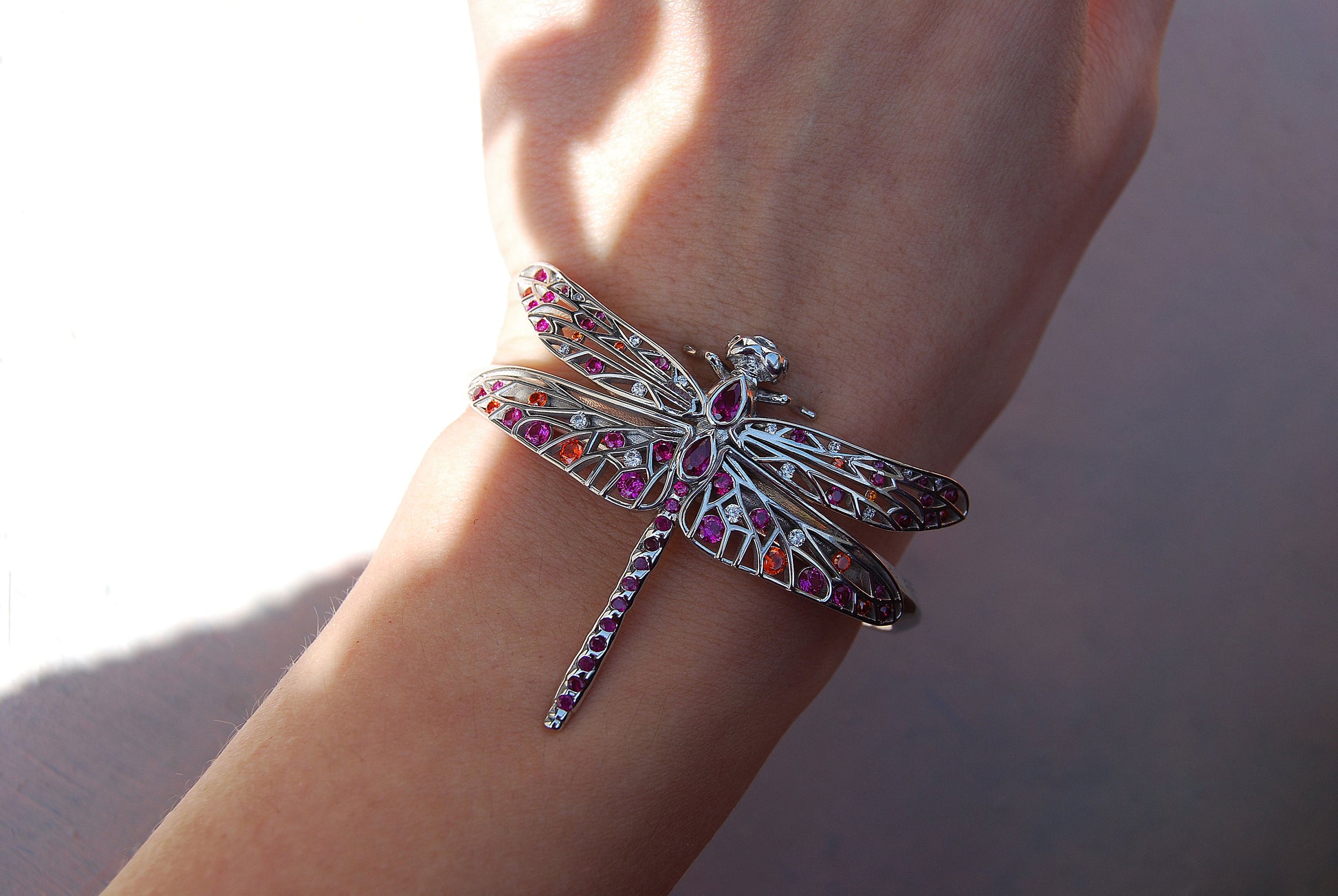 Woman wearing sterling silver dragonfly bracelet with red, pink, orange, and white zirconia stones