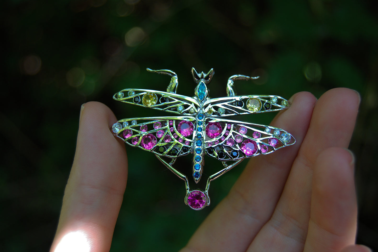 Hand holding silver praying mantis pendant with detailed limbs and polished finish