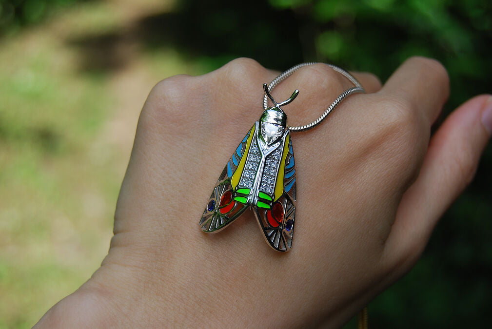 Close-up of Picasso Moth pendant with colorful enamel and zirconia stones resting on hand in natural light