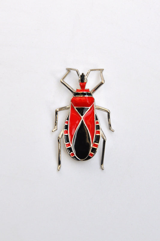 Sterling silver Assassin Bug pendant with red and black enamel, featuring a sculptural insect‑inspired design on a light background.