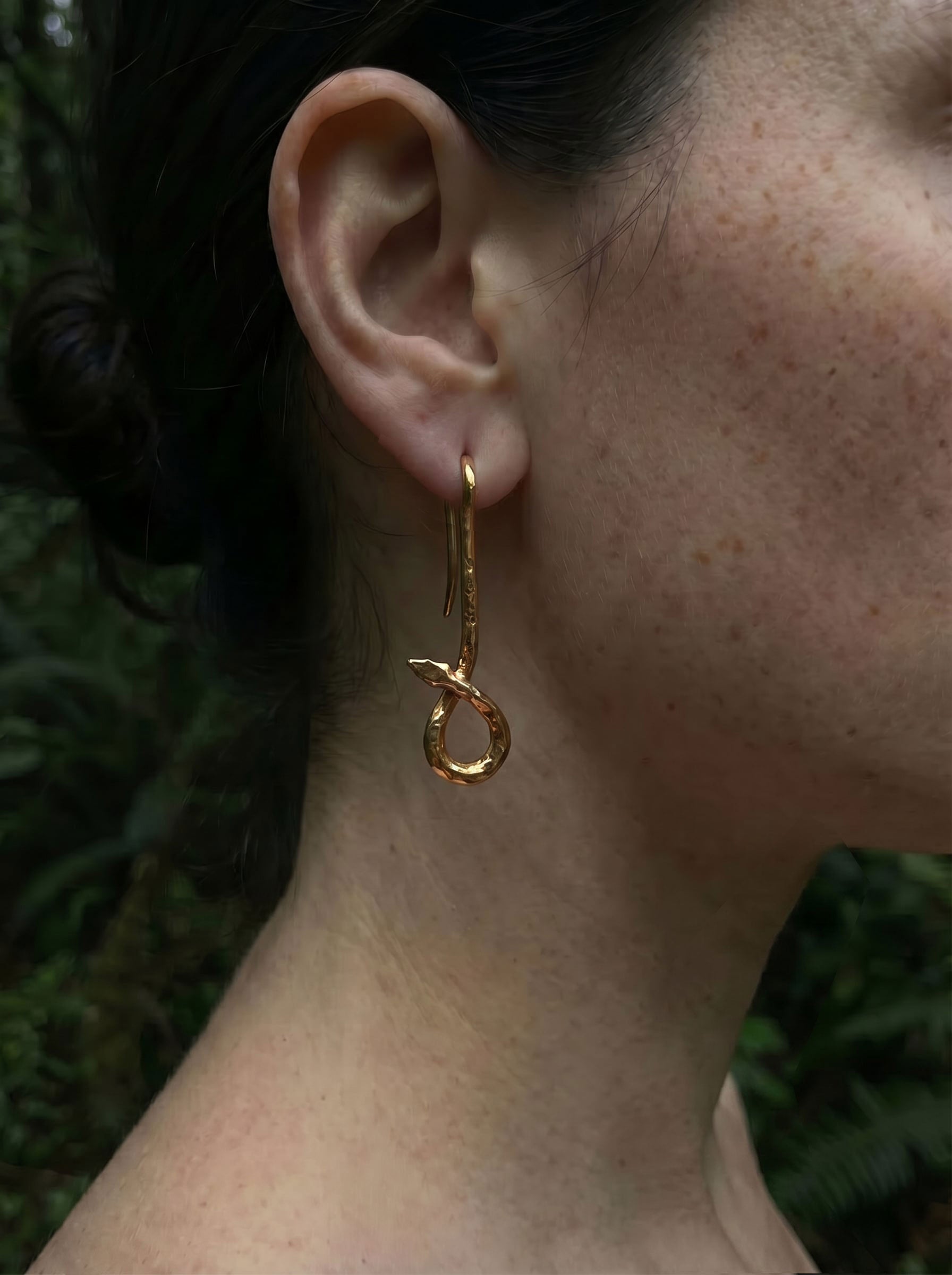 Gold serpent drop earring with engraved texture and sculptural curves, shown on model outdoors.