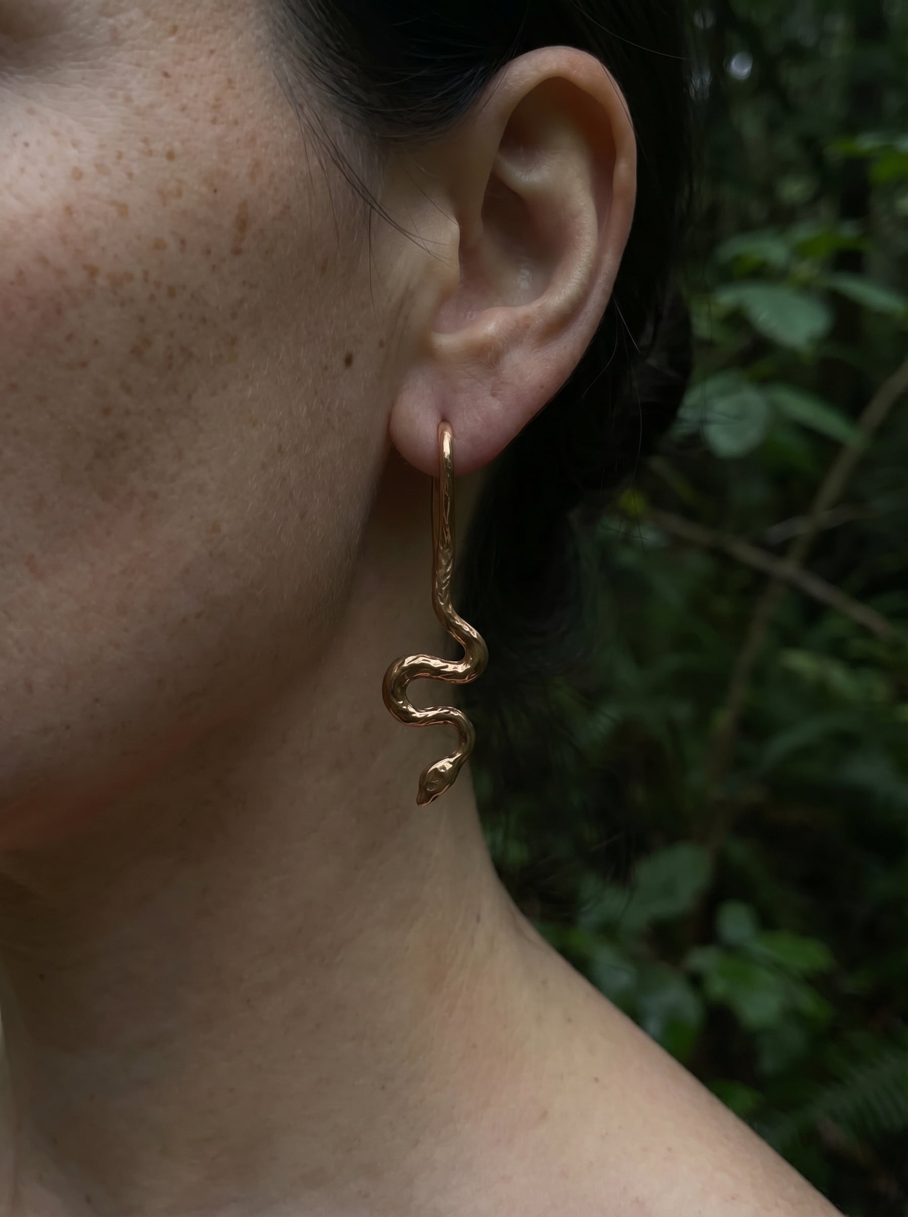 Gold serpent drop earring with engraved texture and sculptural curves, shown on model outdoors.