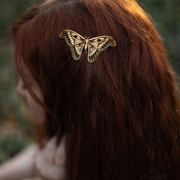 Close-up of model wearing Atlas Moth hair comb in a natural outdoor setting, showcasing handcrafted insect-inspired jewelry with detailed wing design and metallic finish.