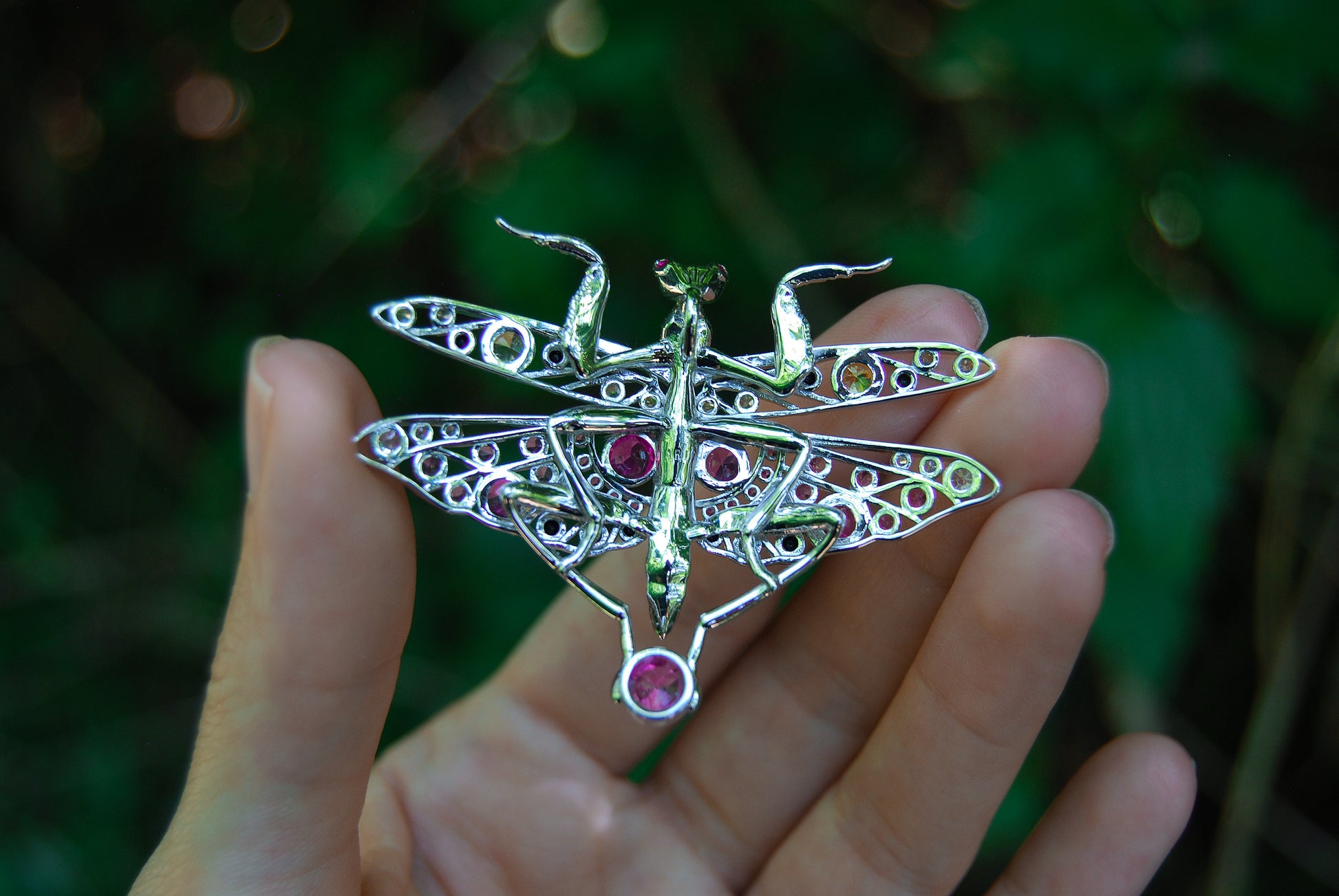 Back view of silver praying mantis pendant held in hand showing clasp and textured detailing