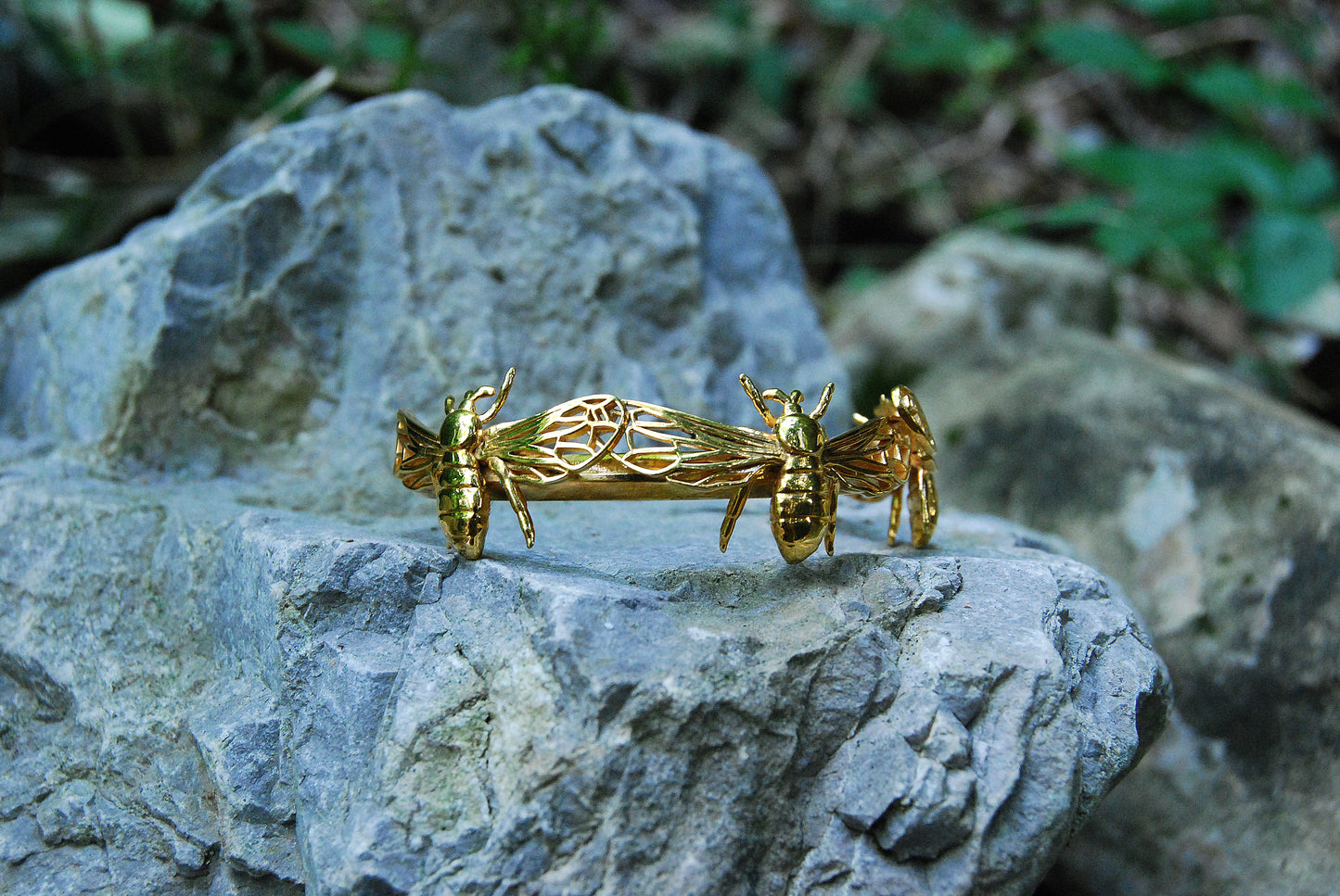 Handmade gold bee cuff bracelet photographed on natural stone background.