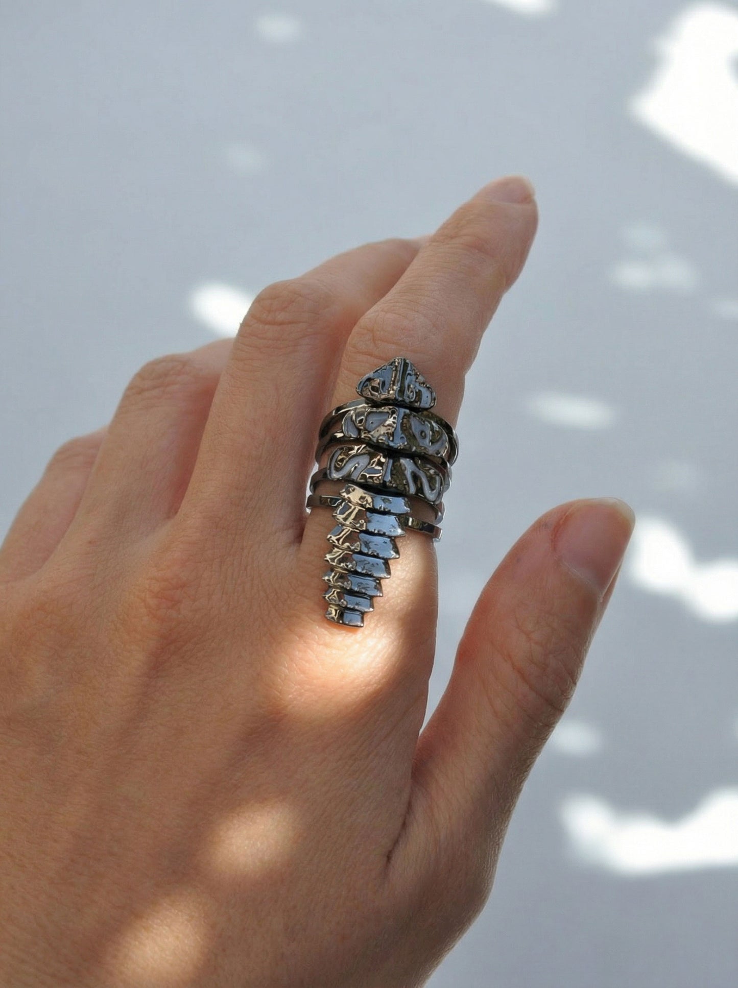 Hand wearing a black rhodium plated trilobite beetle stacking ring set, with four segmented bands forming a sleek, sculptural silhouette.