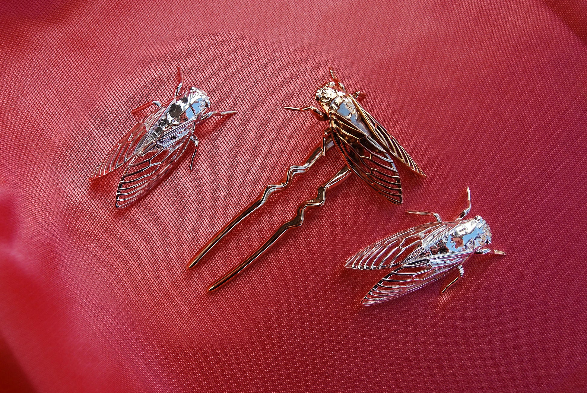 Bronze ant-shaped hair pin and silver cicada pendants arranged on soft silk fabric, highlighting the intricate insect designs and contrasting metallic textures against the smooth, luxurious backdrop.