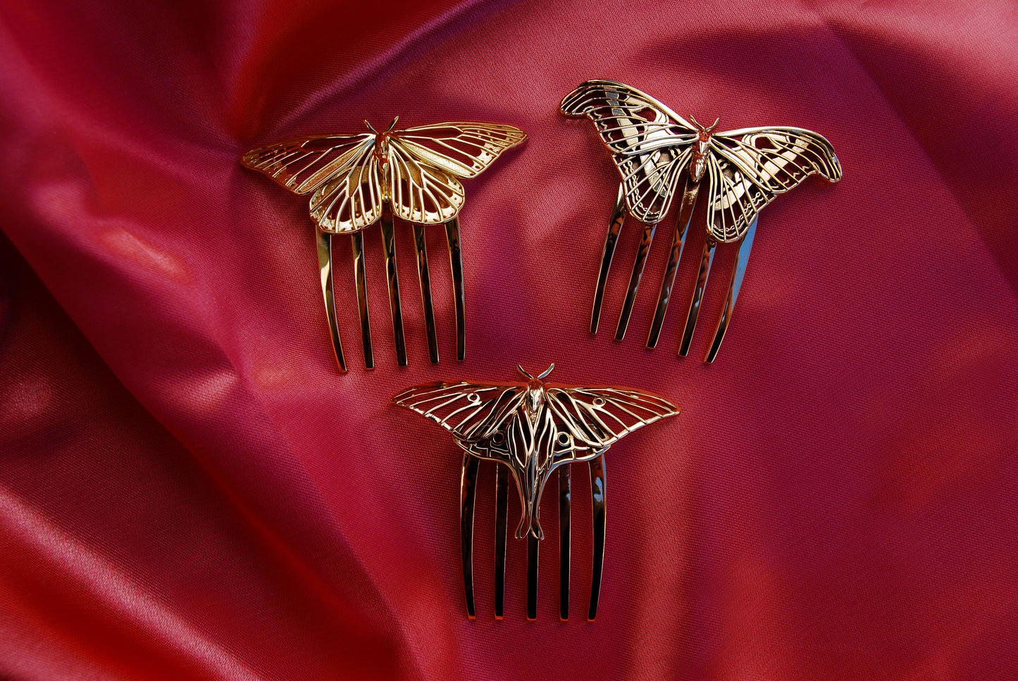 Luna Moth and Atlas Moth hair combs in polished bronze alongside a 14k gold plated Monarch Butterfly comb, arranged on a soft pink silk background to highlight their elegant insect-inspired jewelry design.