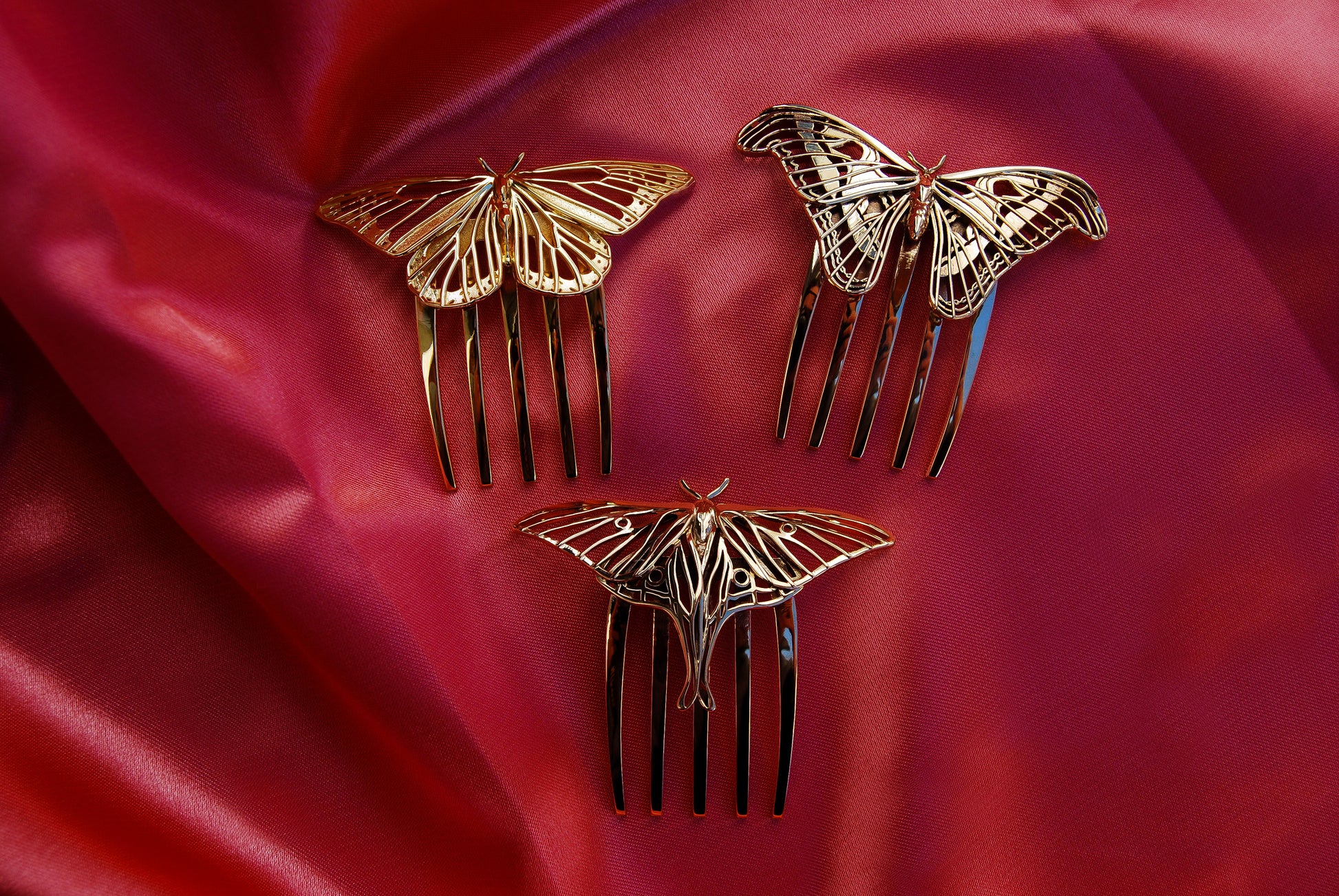 Luna Moth and Atlas Moth hair combs in polished bronze alongside a 14k gold plated Monarch Butterfly comb, arranged on a soft pink silk background to highlight their elegant insect-inspired jewelry design.