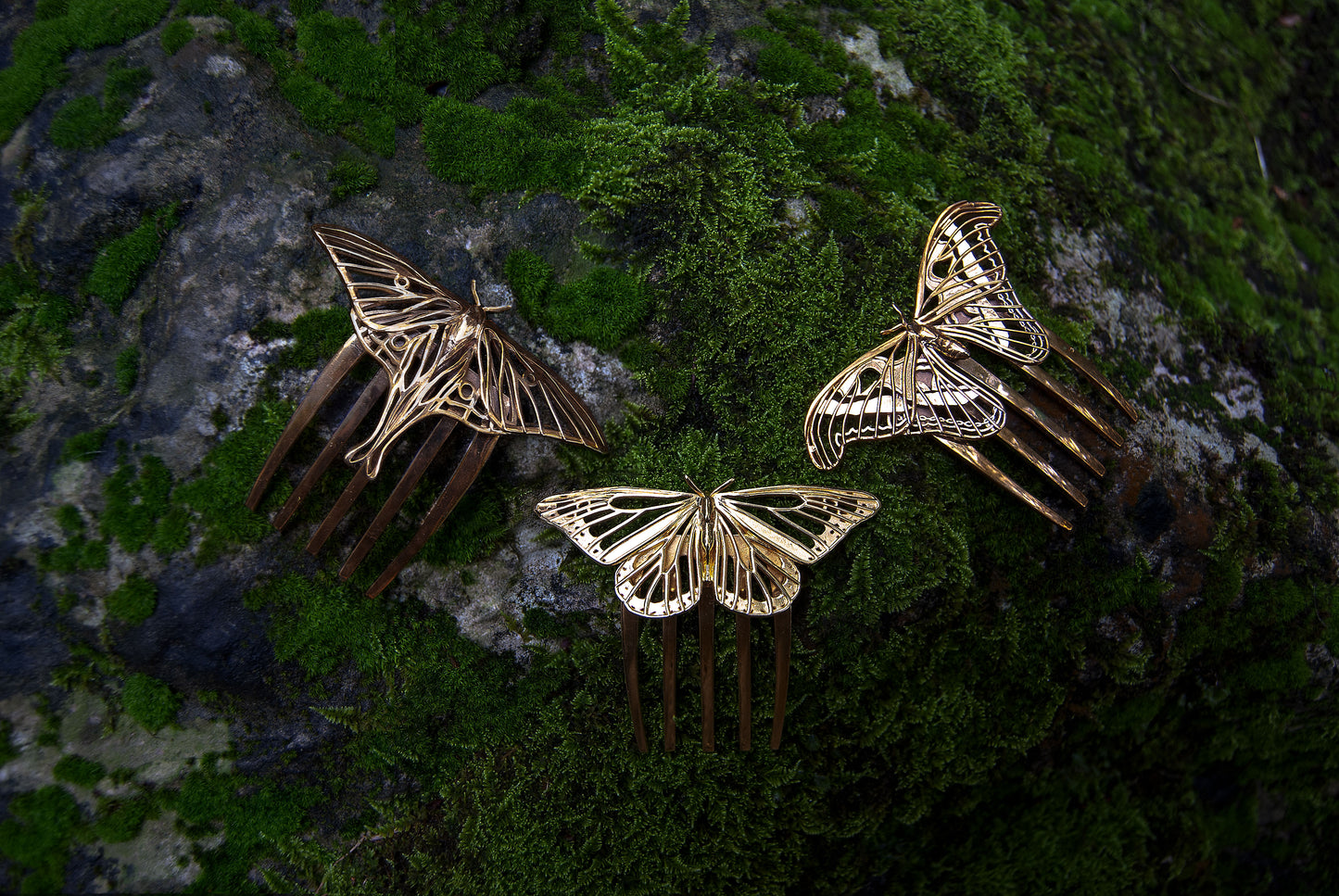 Luna Moth and Atlas Moth hair combs in polished bronze alongside a 14k gold plated Monarch Butterfly comb, displayed in a forest setting to highlight their nature-inspired insect jewelry design.