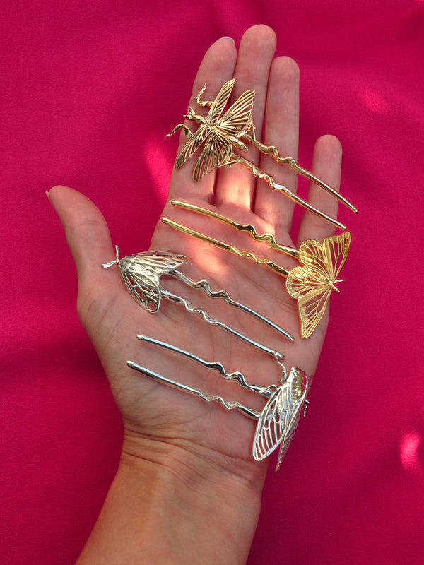 Hand holding gold hair pins against a pink background
