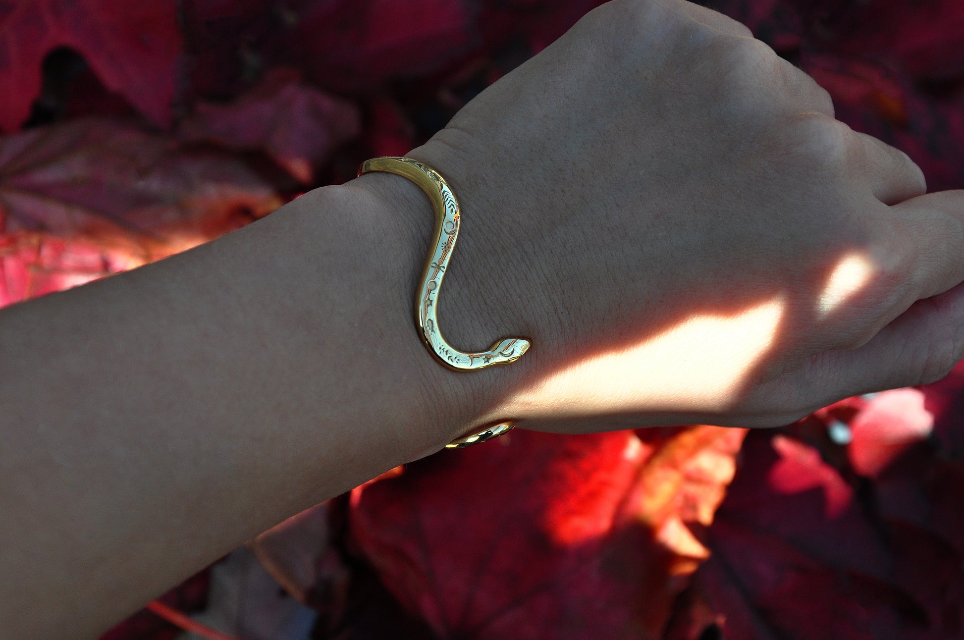 Close‑up of celestial snake bracelet in polished gold, resting on red autumn leaves, designed in Italy.