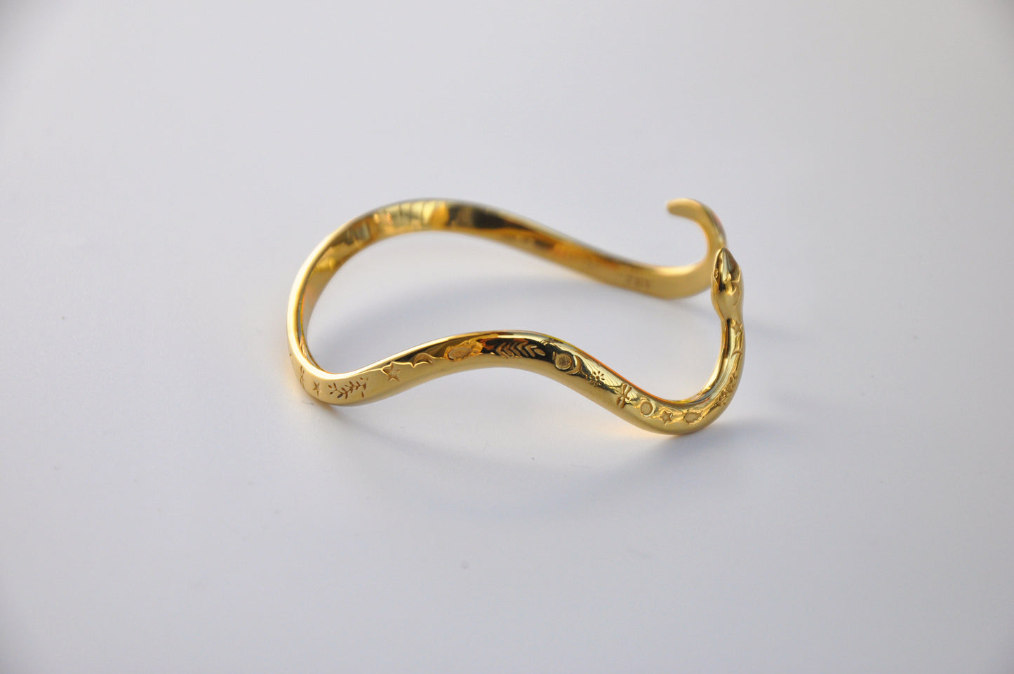 Gold celestial snake bracelet photographed on a clean white background, showing polished texture and engraved details.