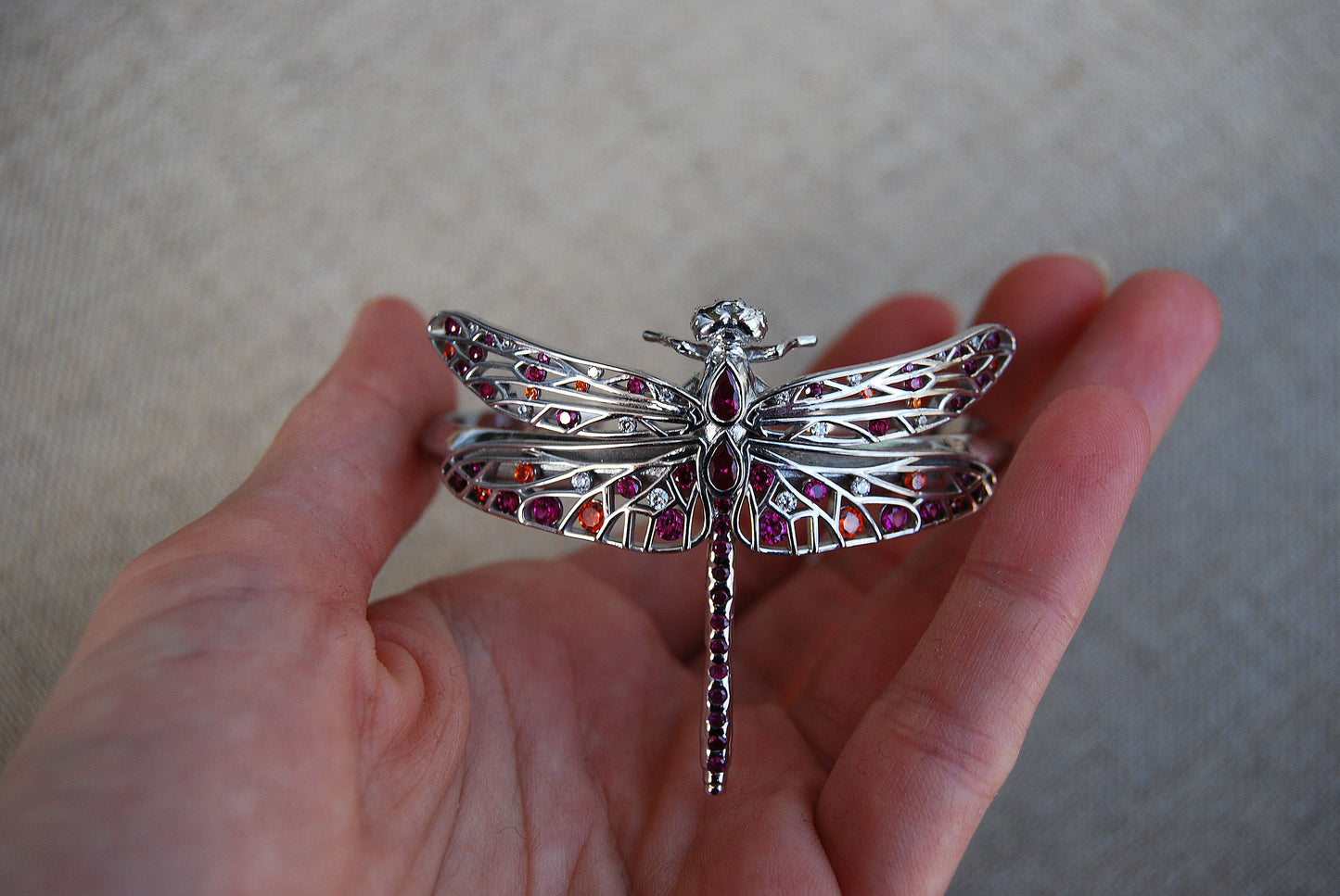 Close-up of a hand holding a dragonfly bracelet with delicate wing details and metallic finish.