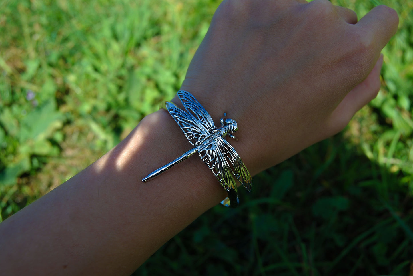 Silver Dragonfly Bracelet worn on hand with green grass background, styled in natural outdoor setting.