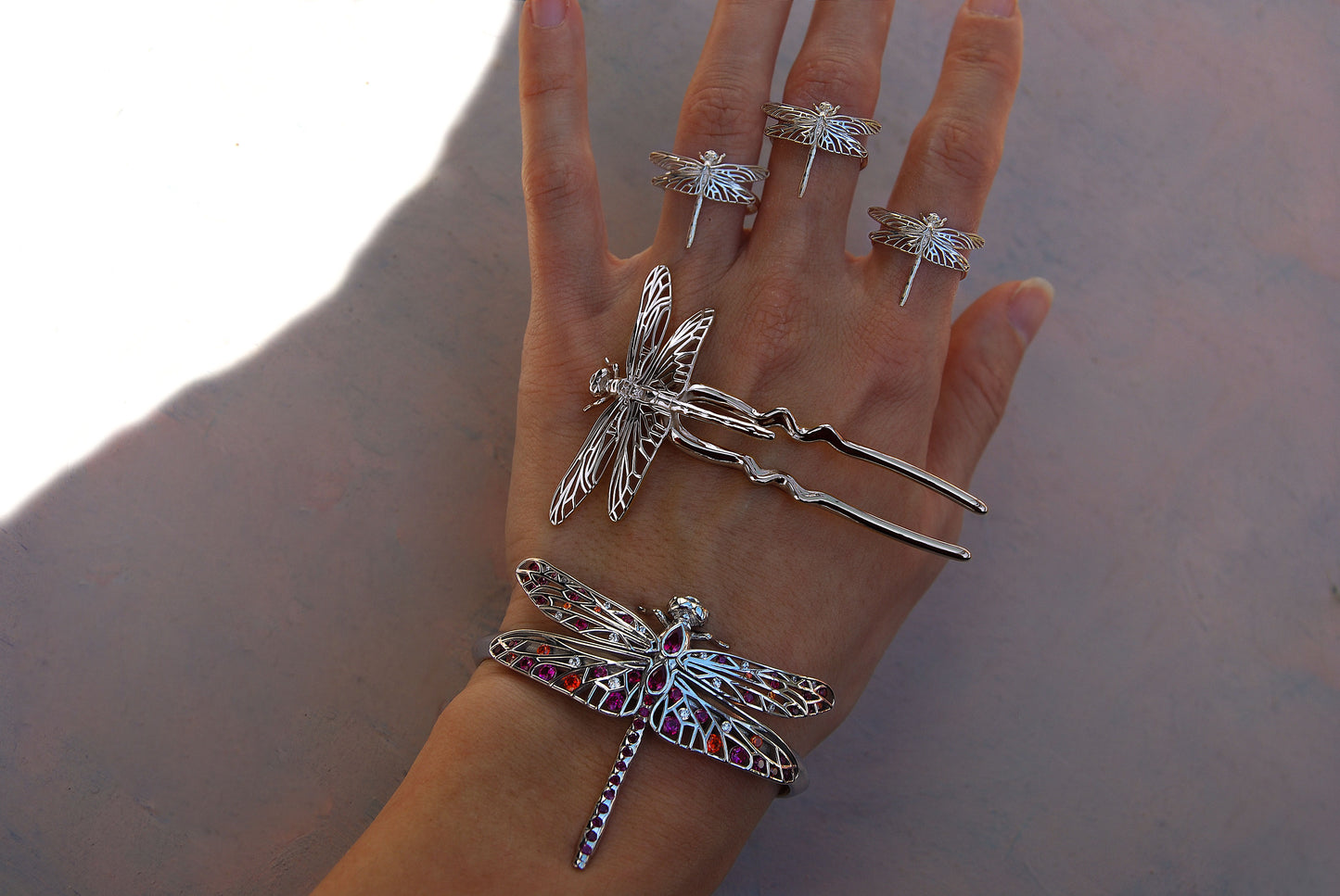 Hand wearing dragonfly-themed jewelry: bracelet, rings, and hair pin with wing motifs