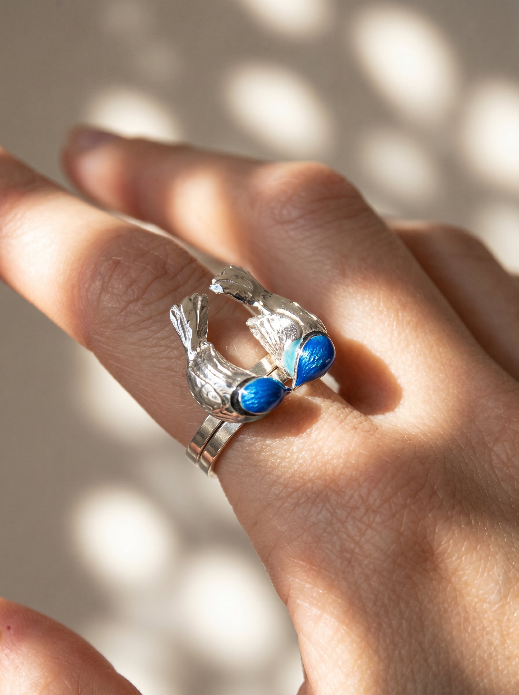 Close-up of Fairy Wren stacking rings on hand, showing two sculpted birds facing each other with vivid blue enamel detail.