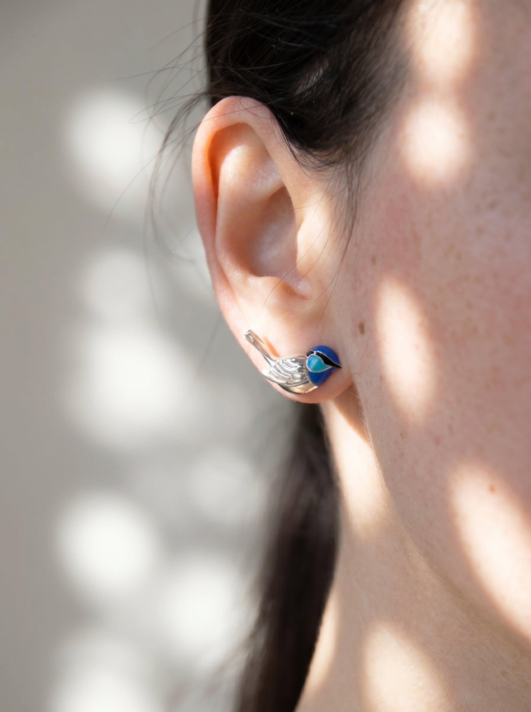 Fairy Wren stud earrings worn on ear in soft natural light, revealing sculptural bird form and iridescent blue enamel.