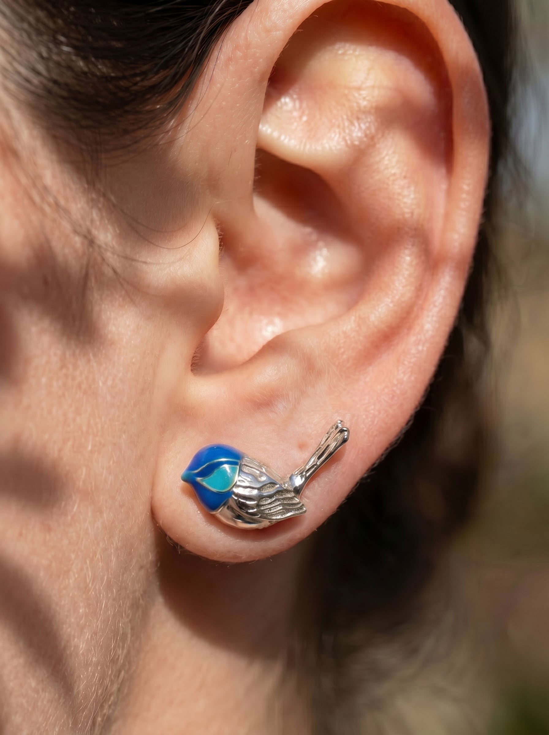 Fairy Wren stud earrings worn on ear in sunlight, highlighting delicate silver craftsmanship and electric turquoise enamel.