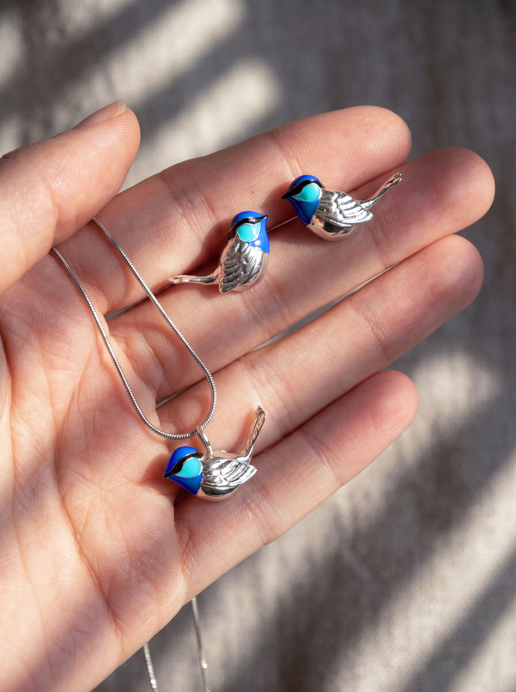 Fairy Wren pendant held in hand, showing vivid blue enamel and sculptural bird silhouette against natural light.