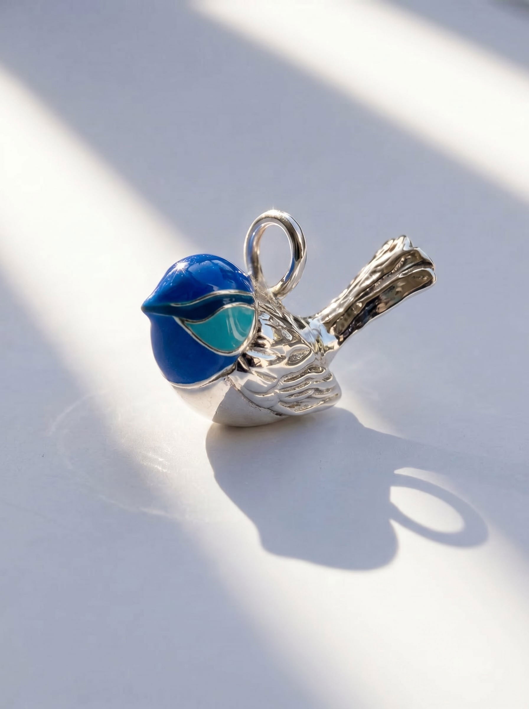 Fairy Wren pendant in sterling silver with hand‑applied blue enamel, photographed in sunlight to reveal sculptural detail and iridescent tones.