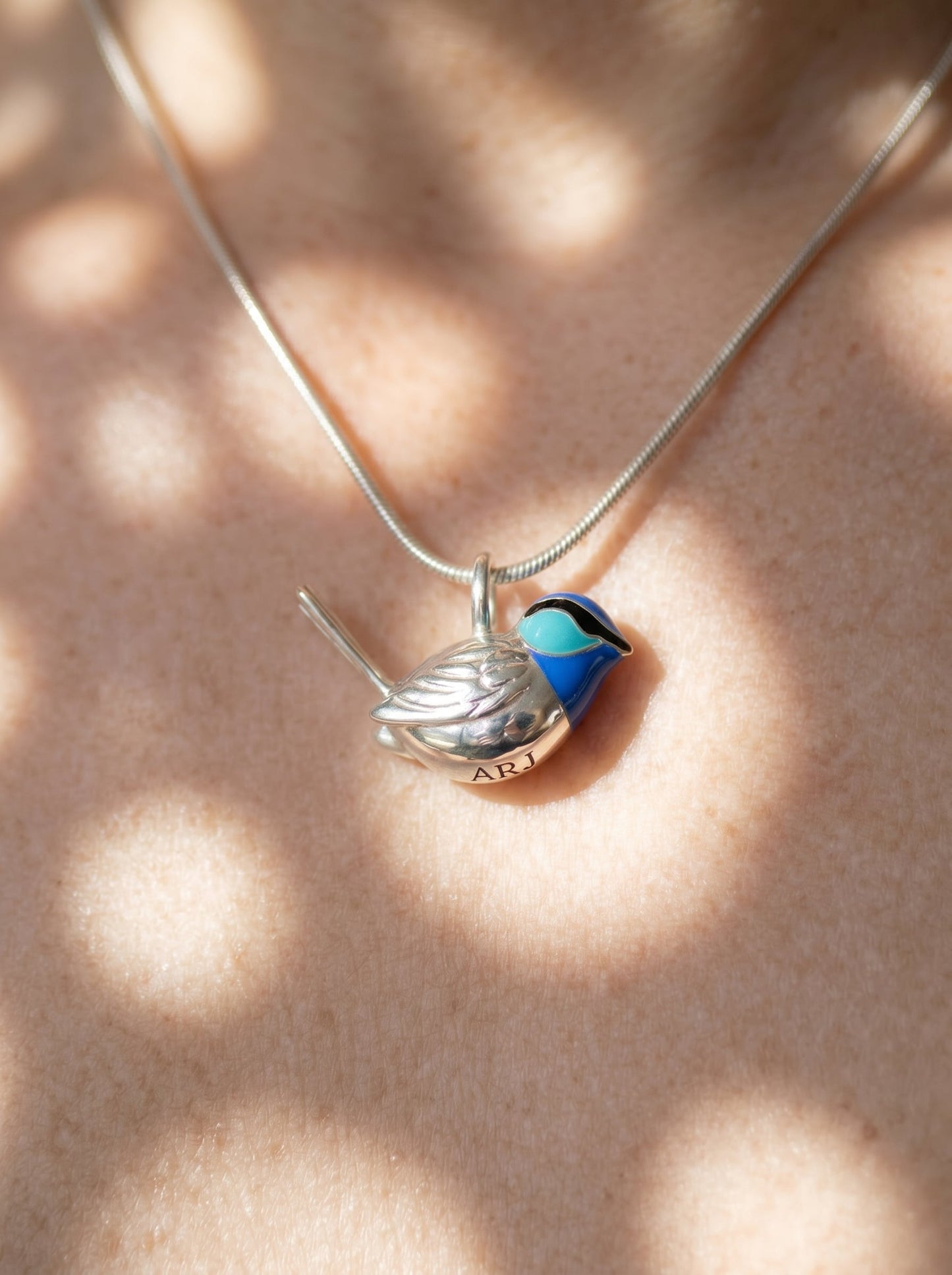 Fairy Wren pendant worn on neck, showing delicate silver bird form and luminous blue enamel under soft light.