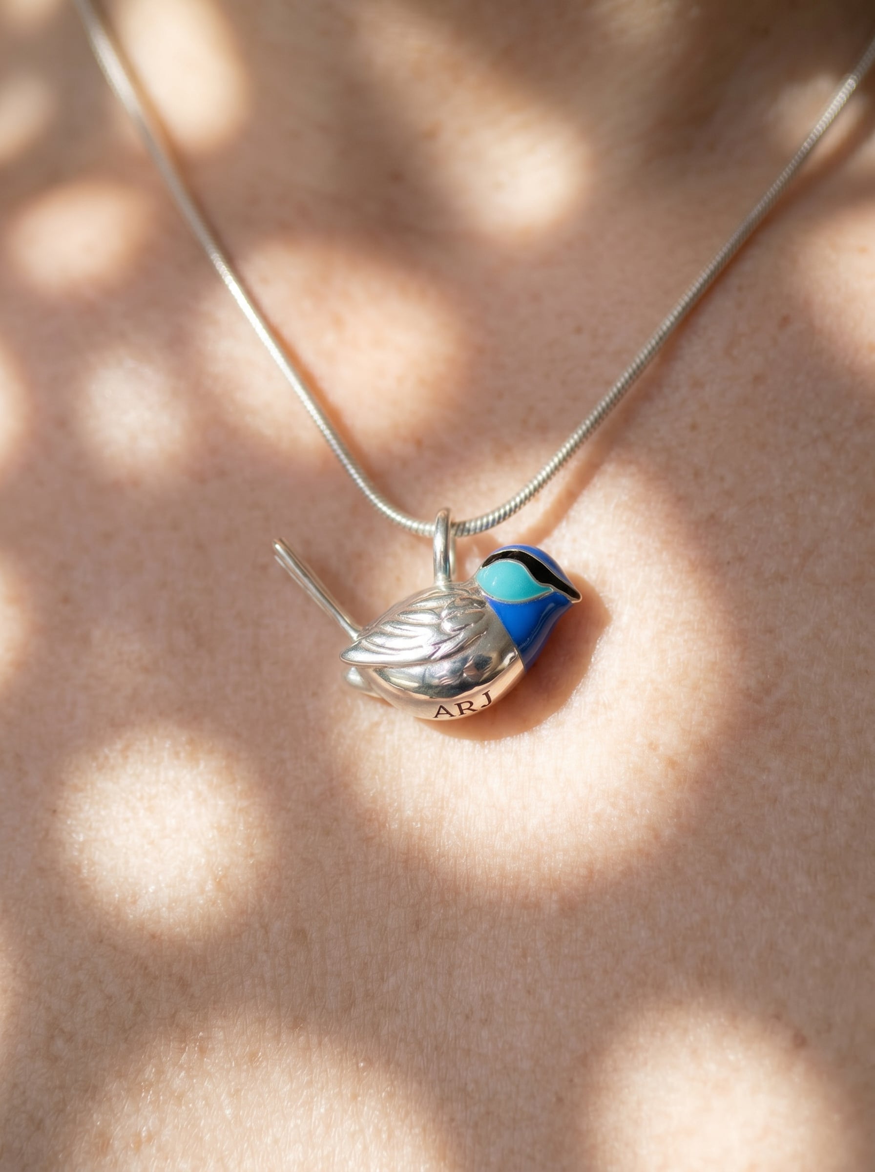 Fairy Wren pendant worn on neck, showing delicate silver bird form and luminous blue enamel under soft light.