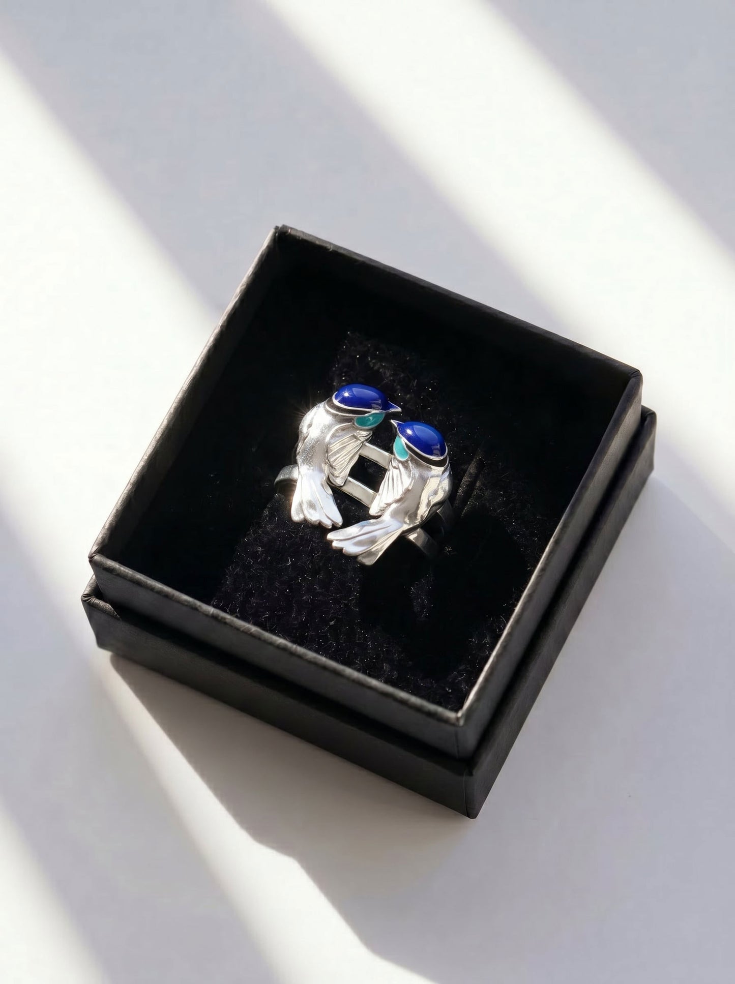 Fairy Wren stacking rings in gift box with natural light reflections, emphasizing artisanal silver and layered enamel.
