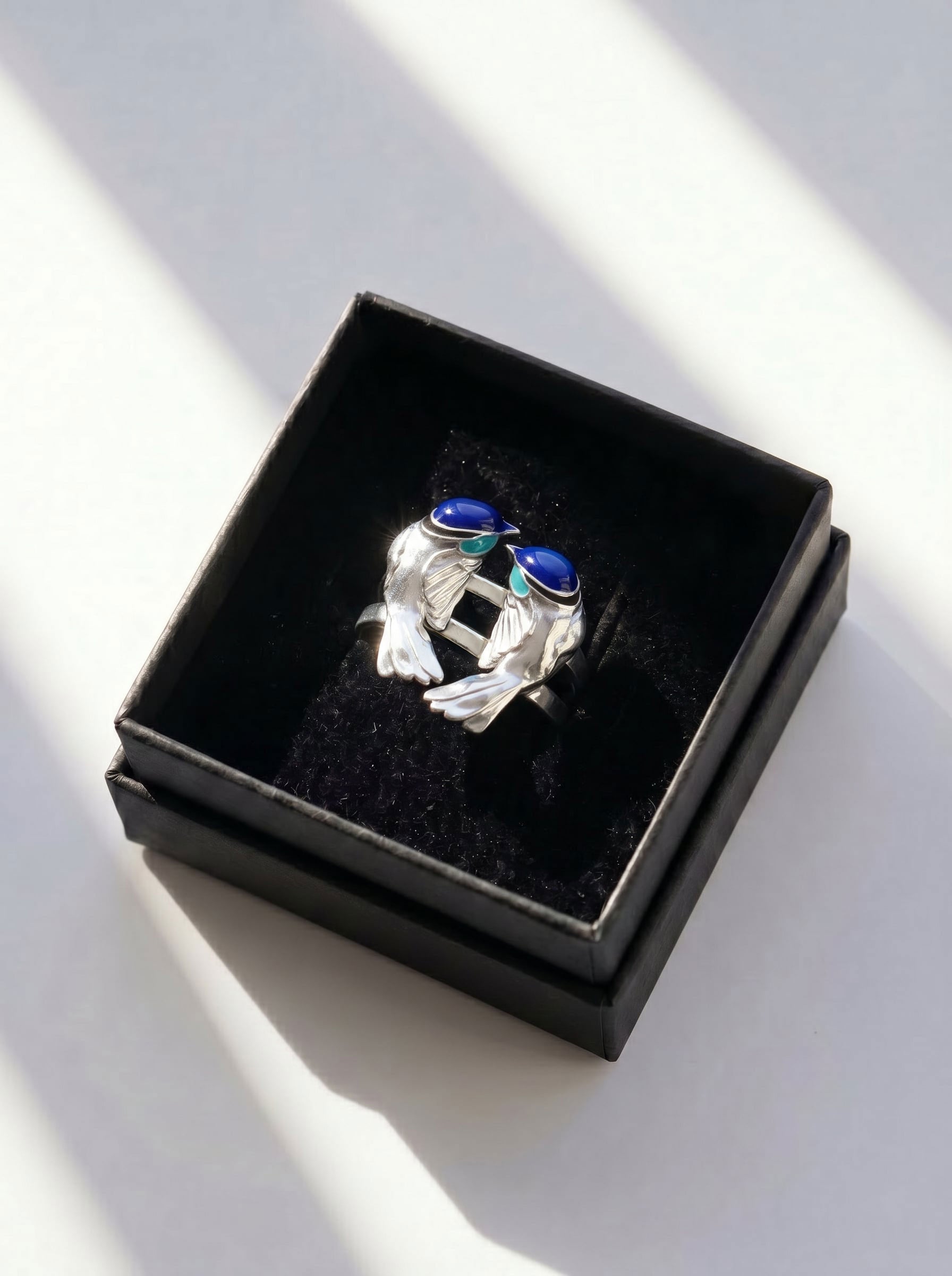 Fairy Wren stacking rings in gift box with natural light reflections, emphasizing artisanal silver and layered enamel.