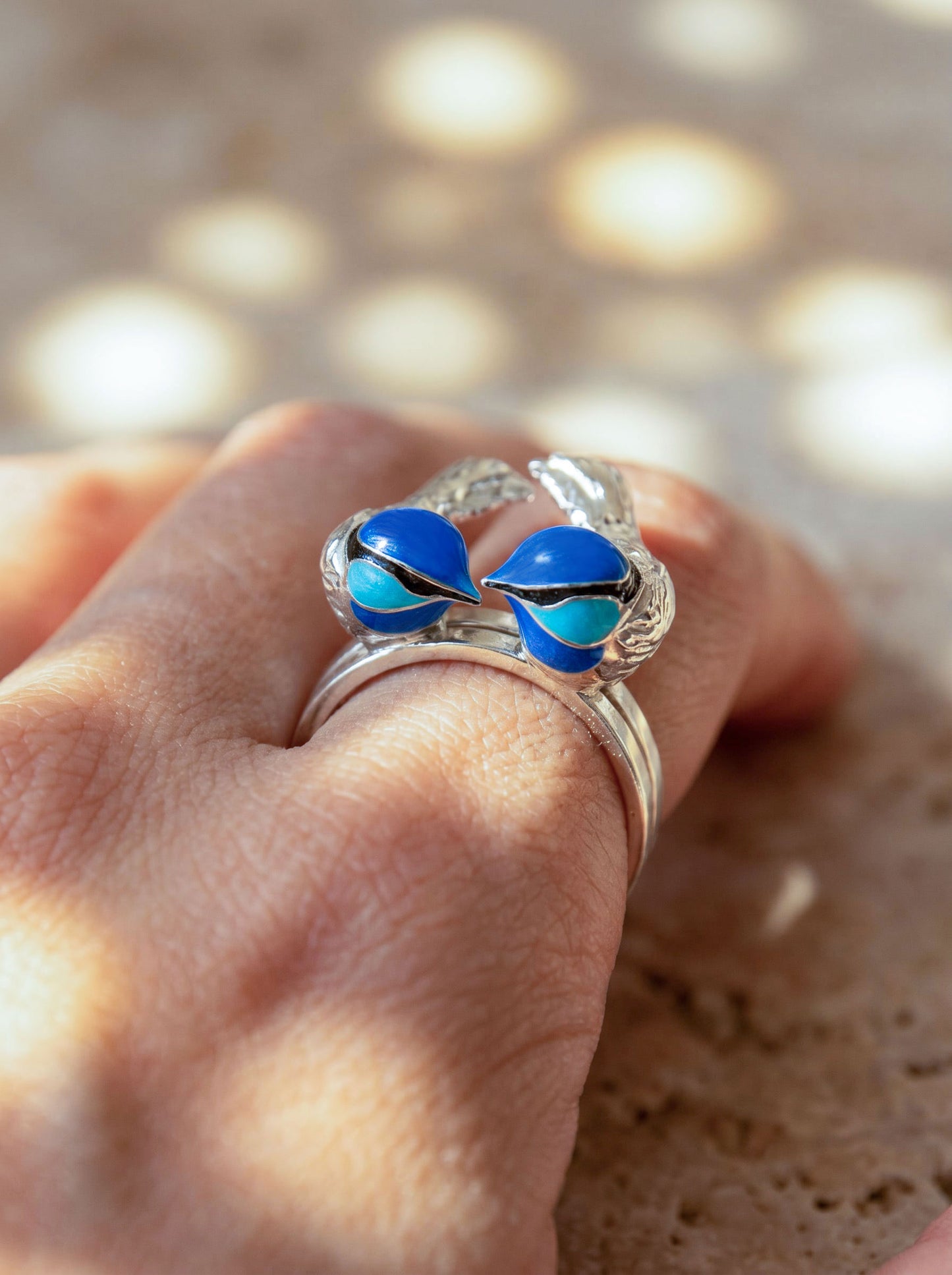 Fairy Wren stacking rings worn on hand under sunlight, highlighting sculptural silver detail and deep blue enamel tones.