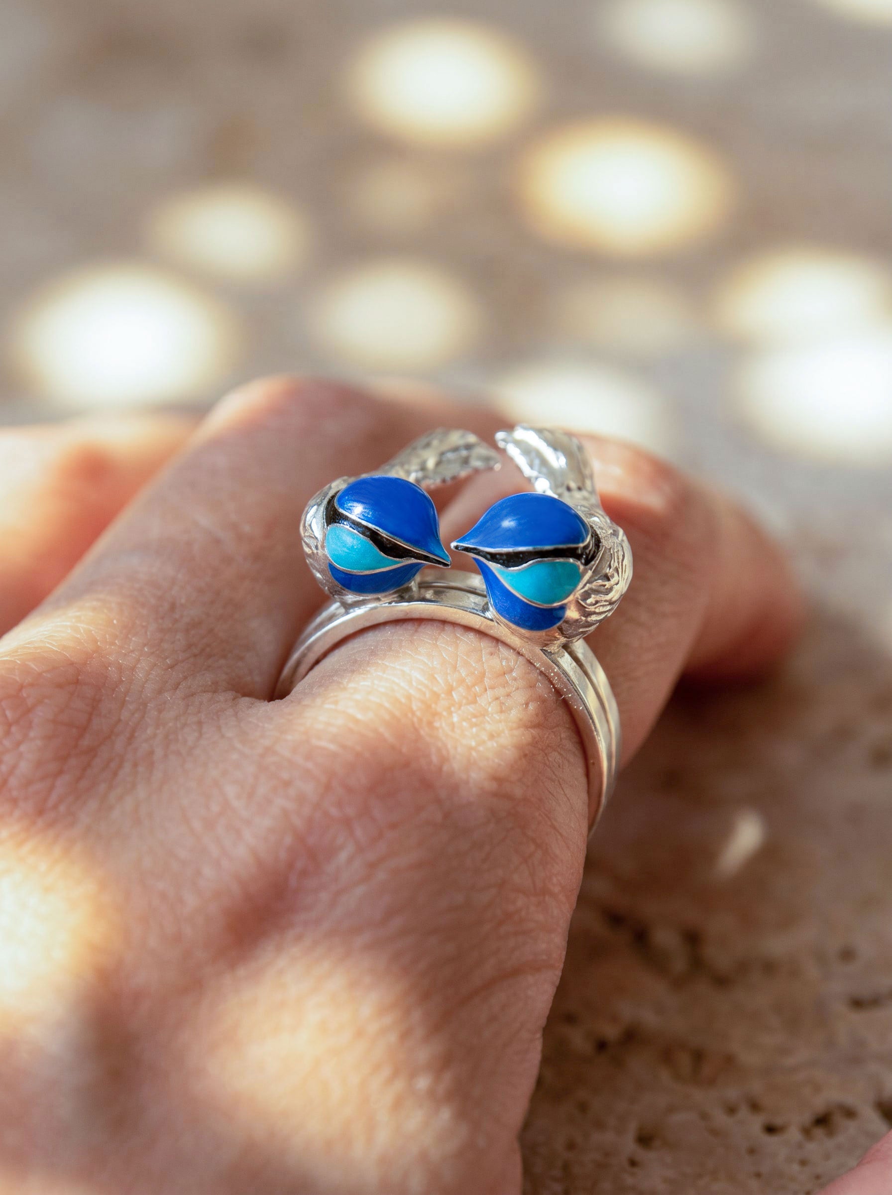 Fairy Wren stacking rings worn on hand under sunlight, highlighting sculptural silver detail and deep blue enamel tones.