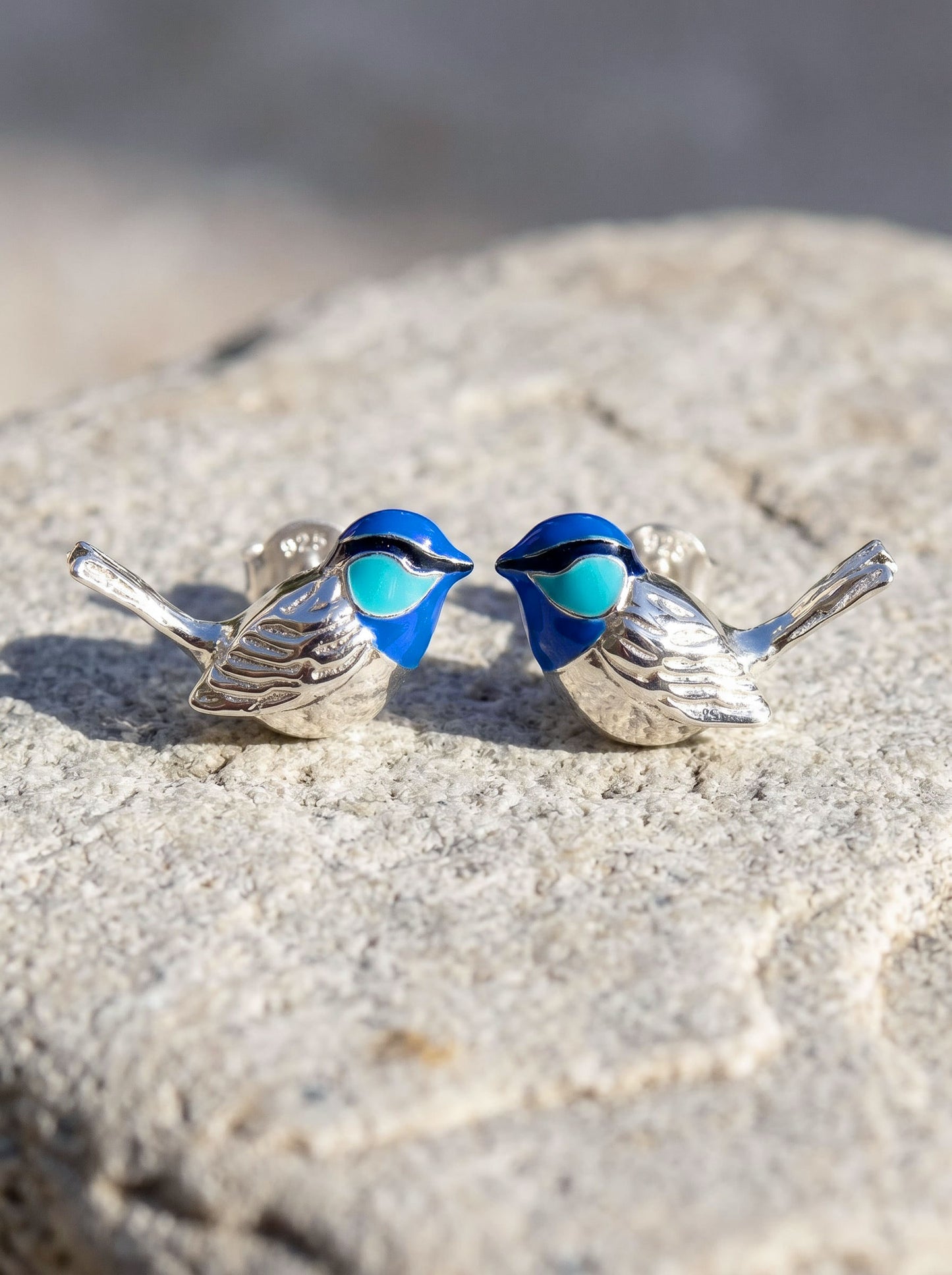 Fairy Wren stud earrings in sterling silver with hand‑enameled blue birds resting on stone, showing sculptural detail and vivid enamel tones.