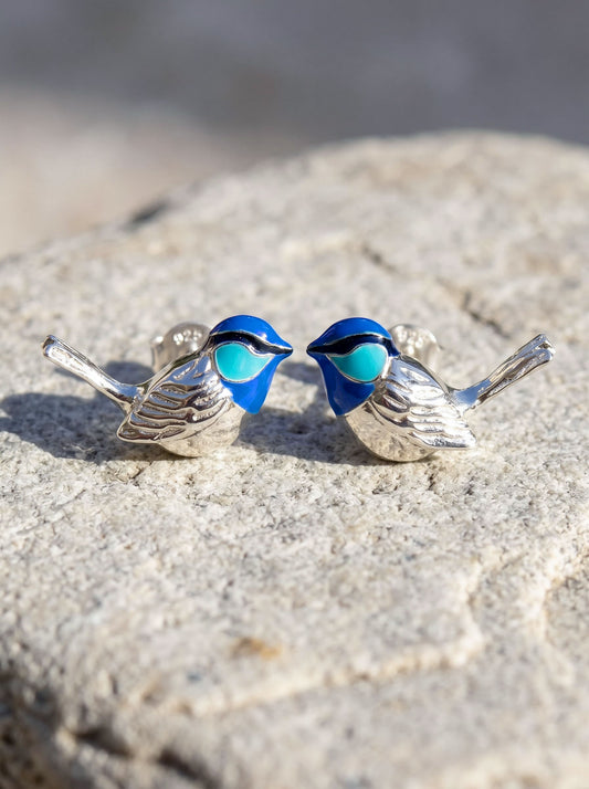 Fairy Wren stud earrings in sterling silver with hand‑enameled blue birds resting on stone, showing sculptural detail and vivid enamel tones.