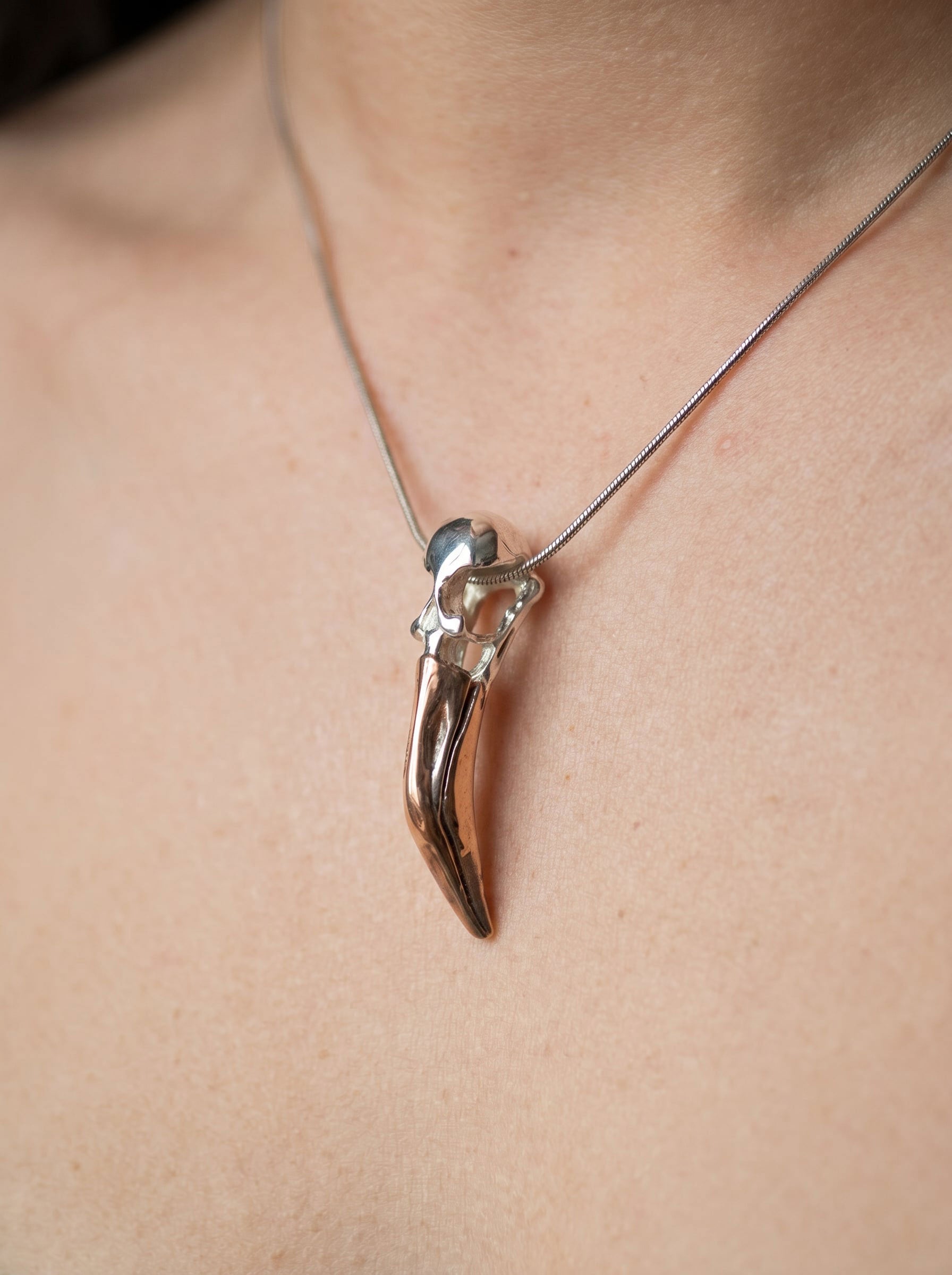 Close-up of Flamingo Skull Pendant worn on neck, showing elongated sculptural skull form in sterling silver with black rhodium and rose-gold accents on a fine chain.