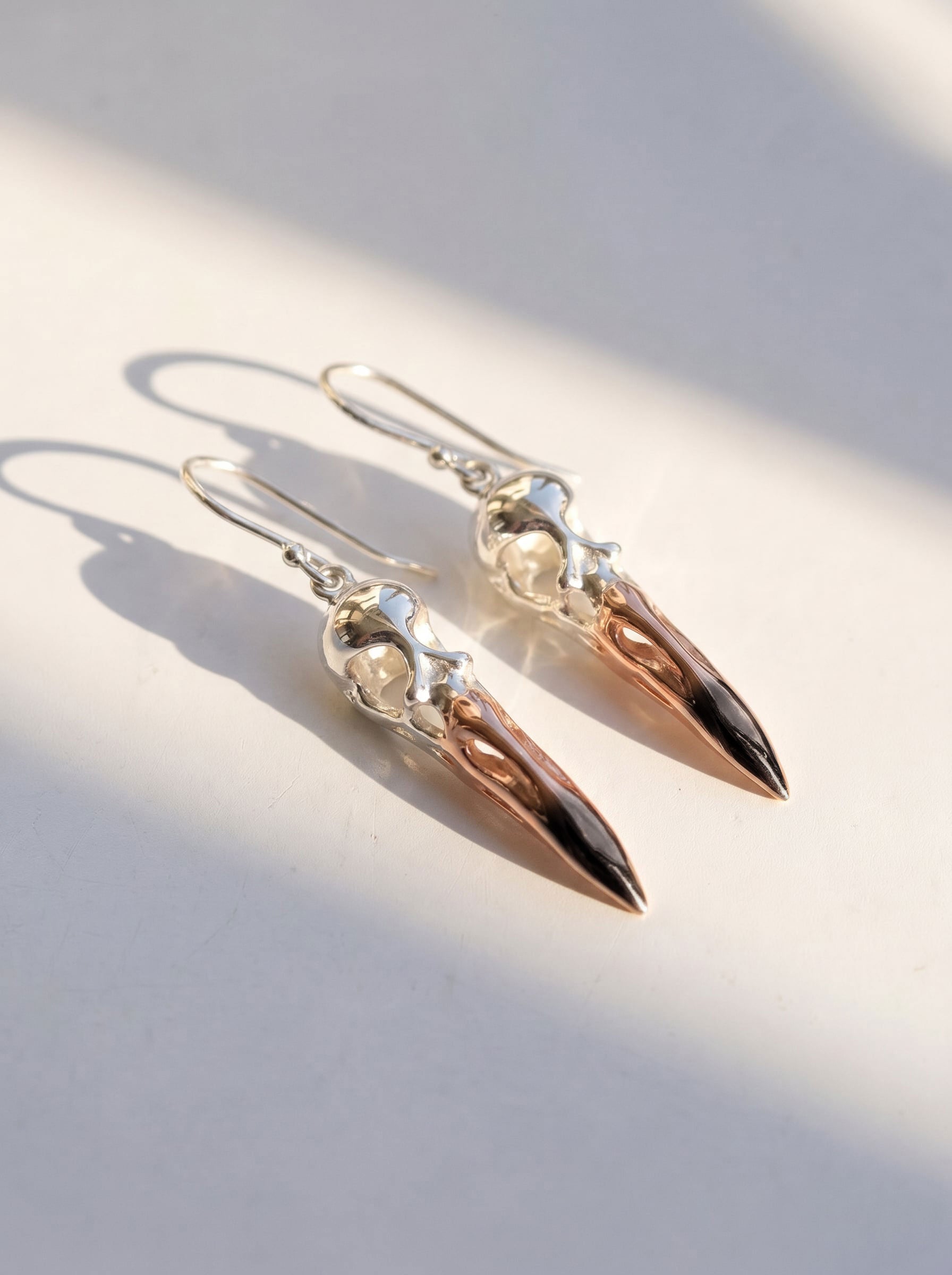 Flamingo Skull Drop Earrings in sterling silver with black rhodium and rose‑gold accents, photographed in sunlight to highlight sculptural form and polished contrast.