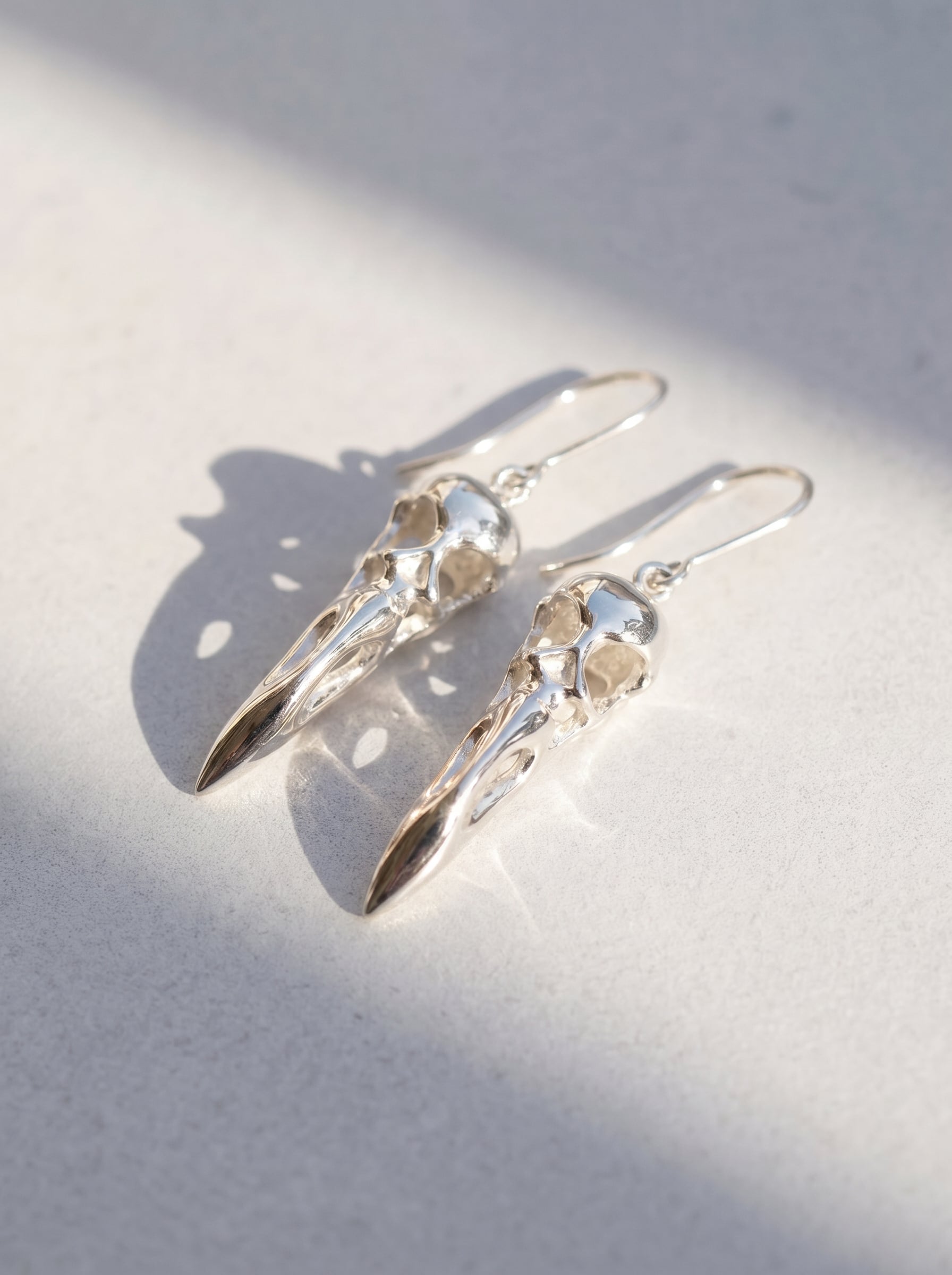 Flamingo Skull Drop Earrings photographed flat on neutral surface, emphasizing anatomical detailing and smooth metallic finish.