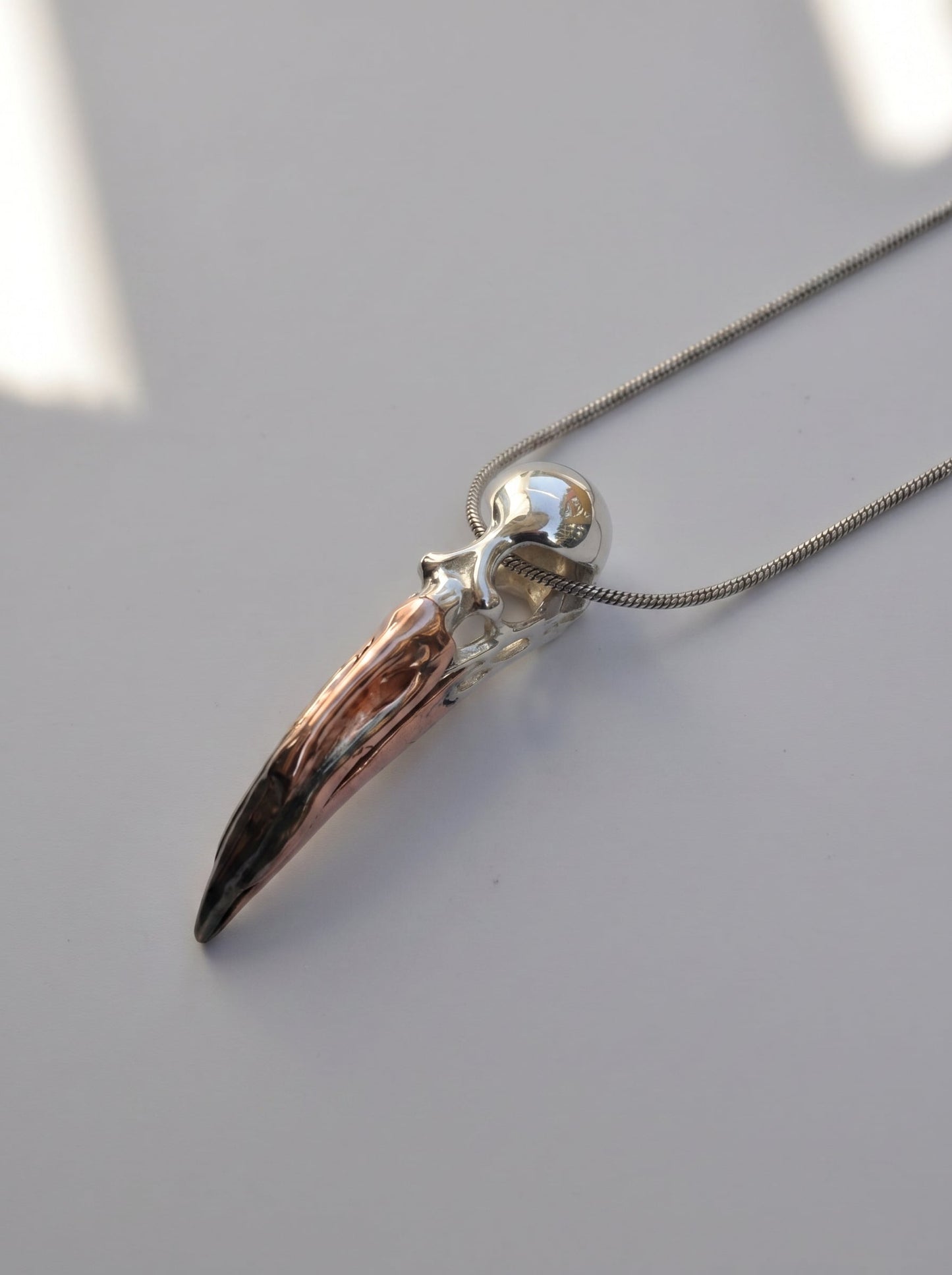Flamingo Skull Pendant photographed flat on neutral surface, showing elongated form and mixed‑metal palette.